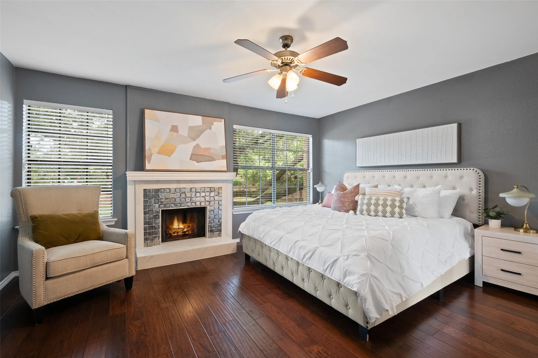 
Primary bedroom showcasing the fireplace, large windows with tree views, hardwood floors, and ample space for a king-size suite — a true retreat within the home.
