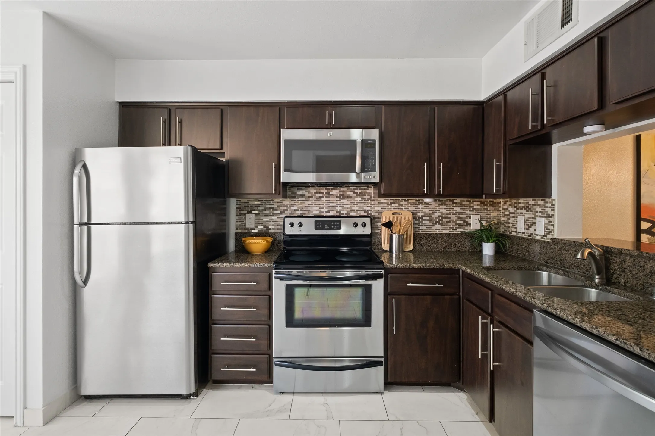 Generous kitchen storage with full-height espresso cabinets, stainless steel appliance suite, granite countertops, and a mosaic tile backsplash running the full width of the cooking wall.
