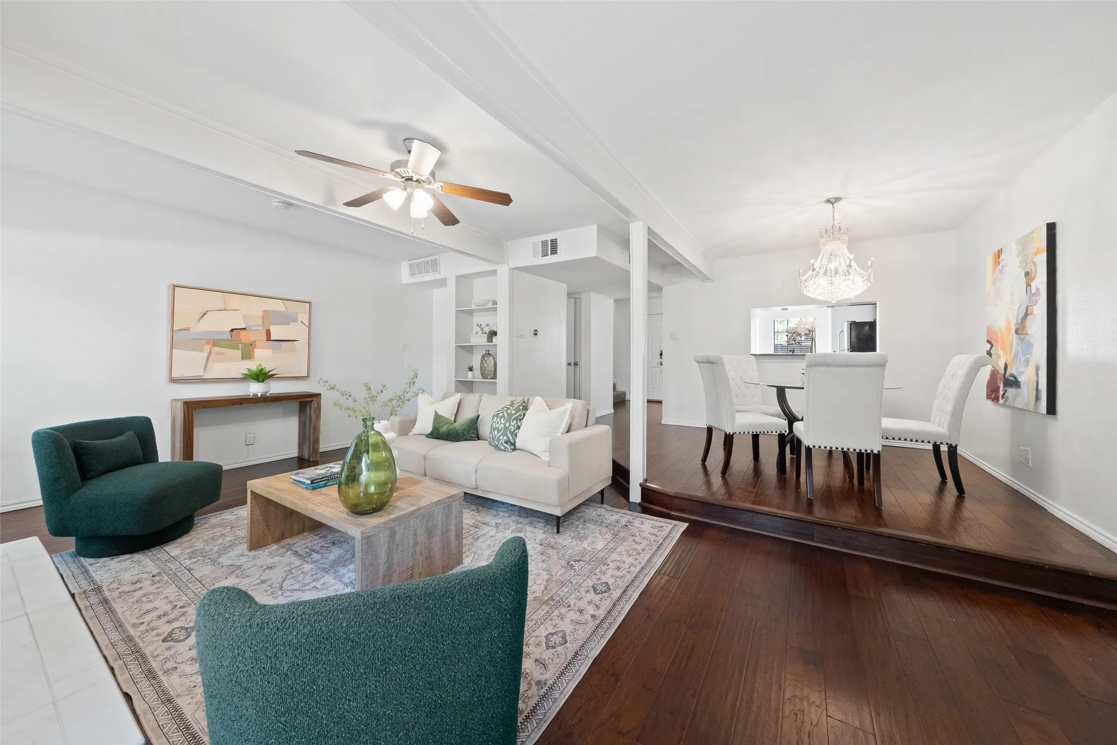Open-concept main level connecting the living room and dining area, with continuous hardwood floors, a crystal chandelier anchoring the dining space, and views straight through to the kitchen.