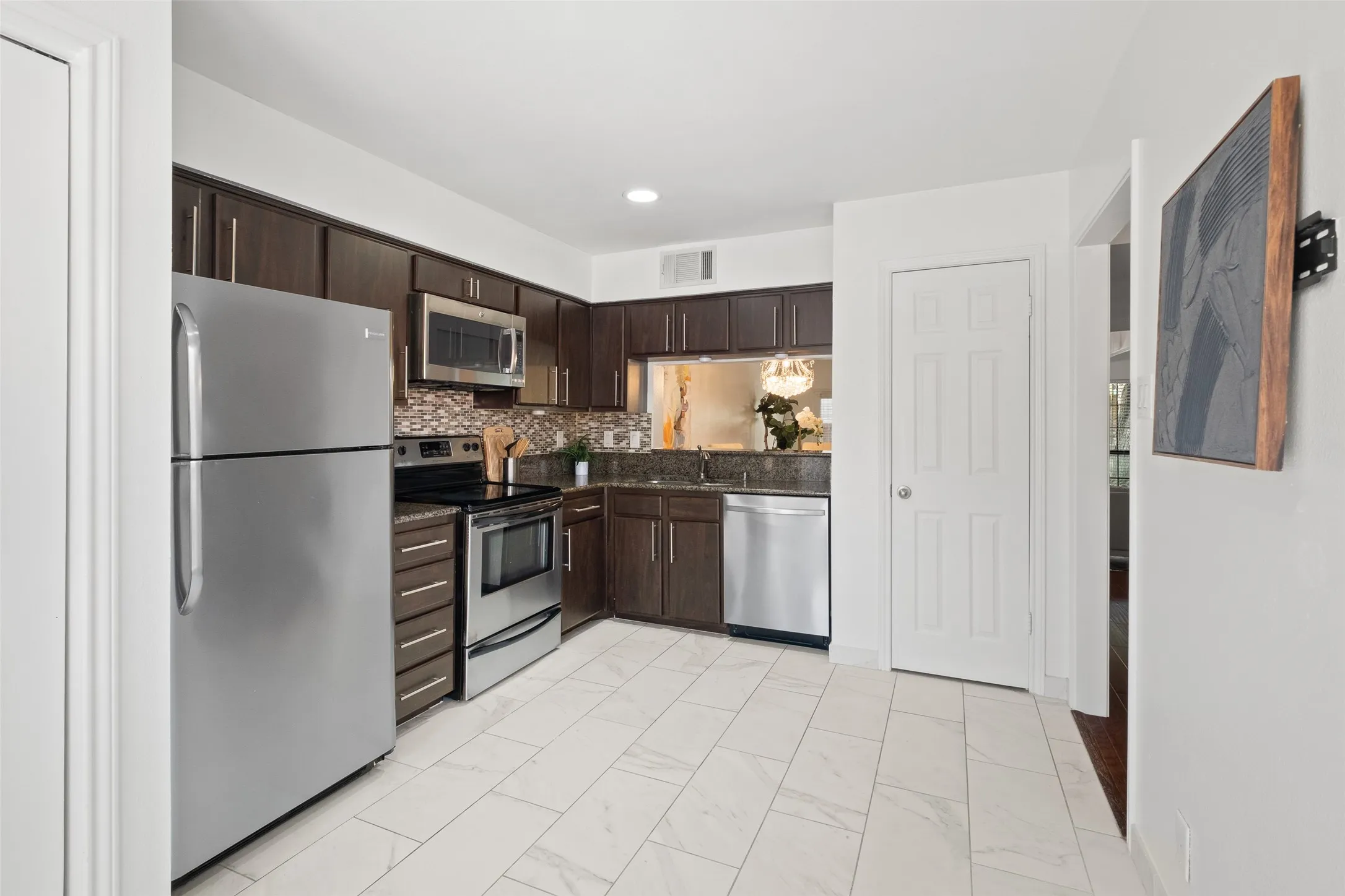 Well-appointed kitchen with full stainless steel appliance package including refrigerator, range, microwave, and dishwasher, complemented by dark cabinetry, granite counters, and a pass-through window to the dining room.