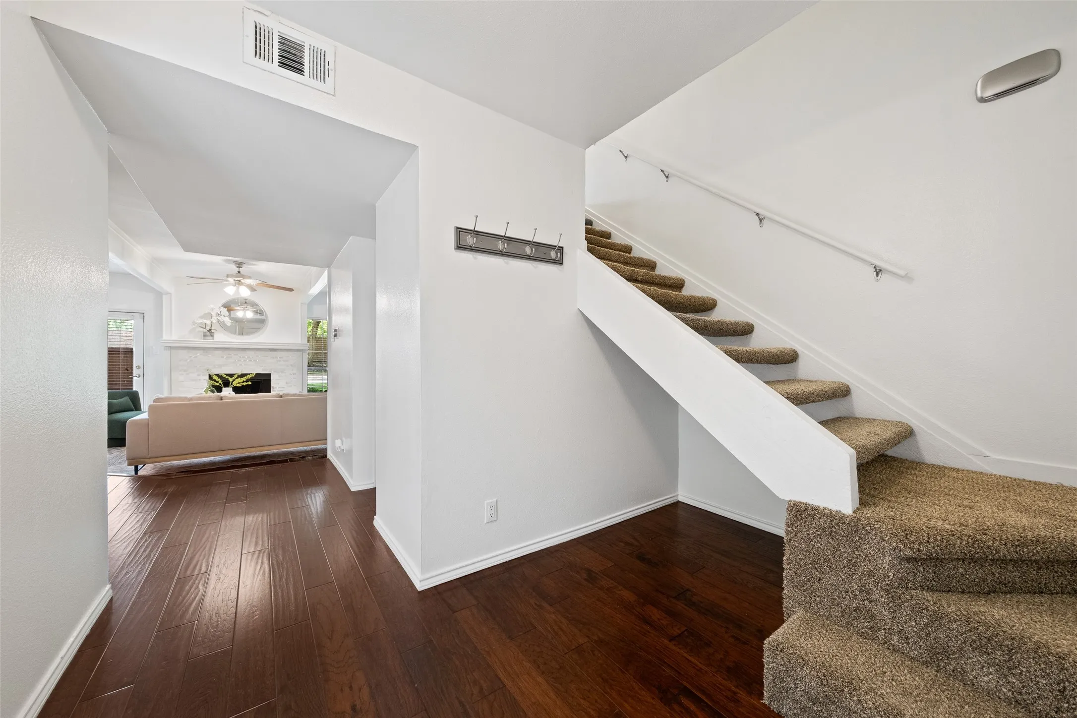 Welcoming entry with hardwood floors, a coat hook landing station, and carpeted staircase leading to the upper level — with a direct view into the living room and fireplace beyond.