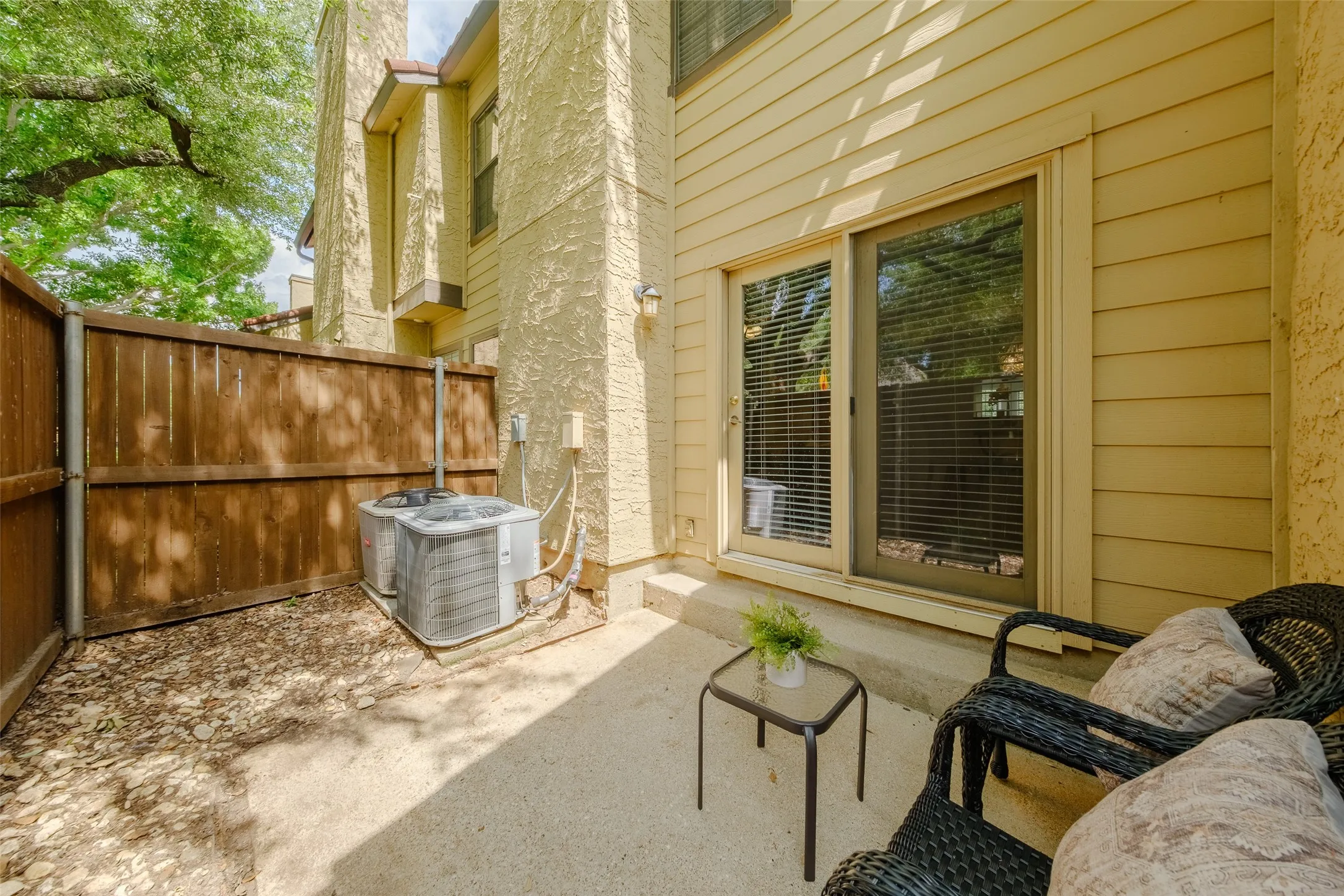 Rear patio with sliding glass door access, fenced privacy, wicker seating area, and established trees providing shade.