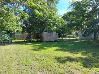 Expansive green yard space featuring mature trees, a wooden fence, and a storage shed