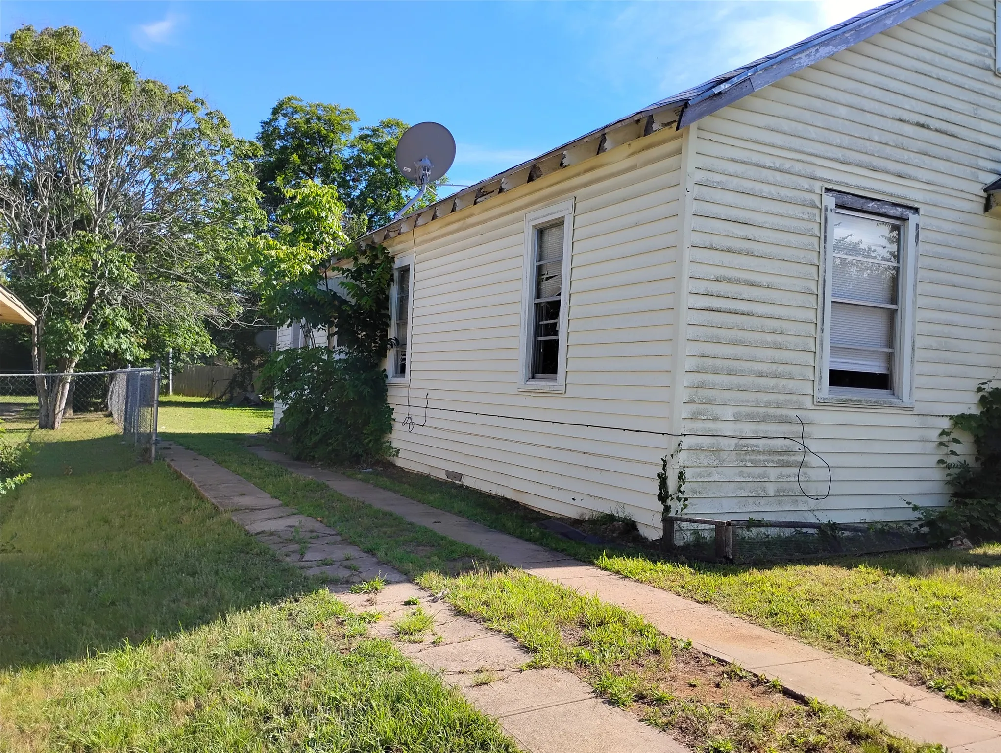 Side exterior featuring horizontal siding, two window openings, and a concrete strip driveway