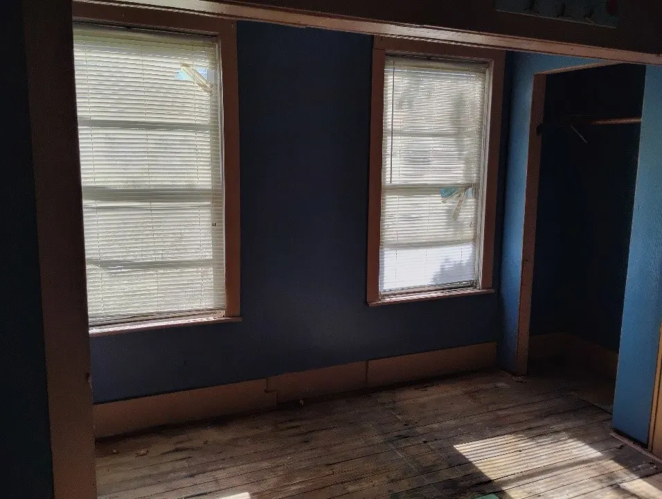 Room featuring two windows with horizontal blinds, wood trim, blue painted walls, and wood-finish flooring