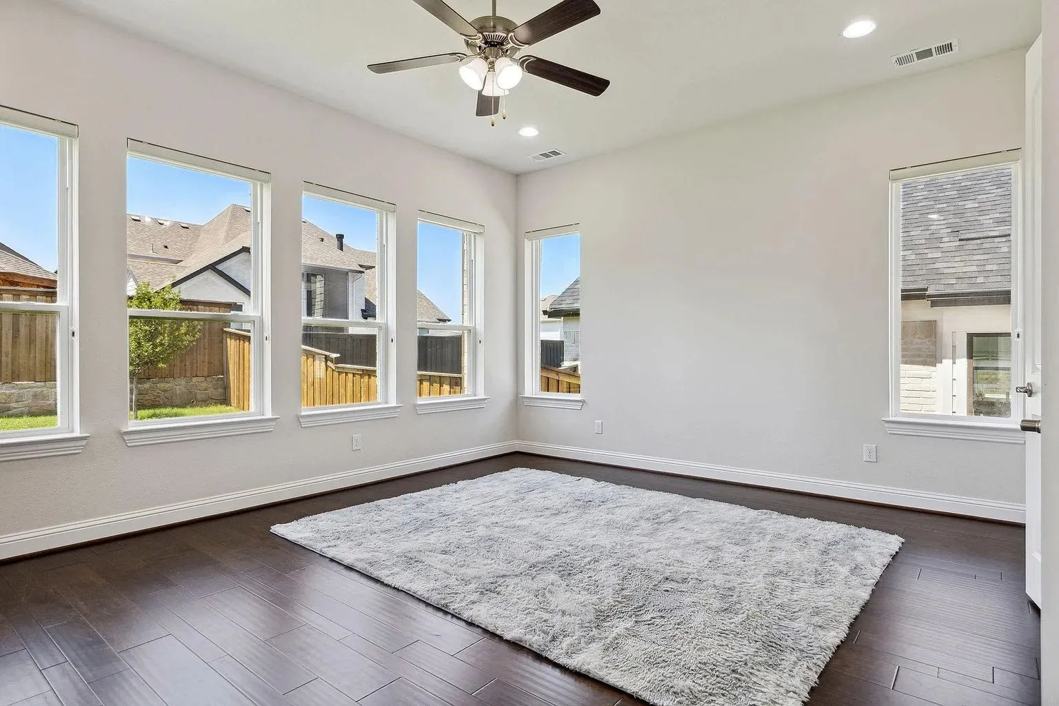 Spacious interior featuring dark wood-finish flooring, multiple large windows, a ceiling fan with integrated lighting, recessed lighting, and white baseboards