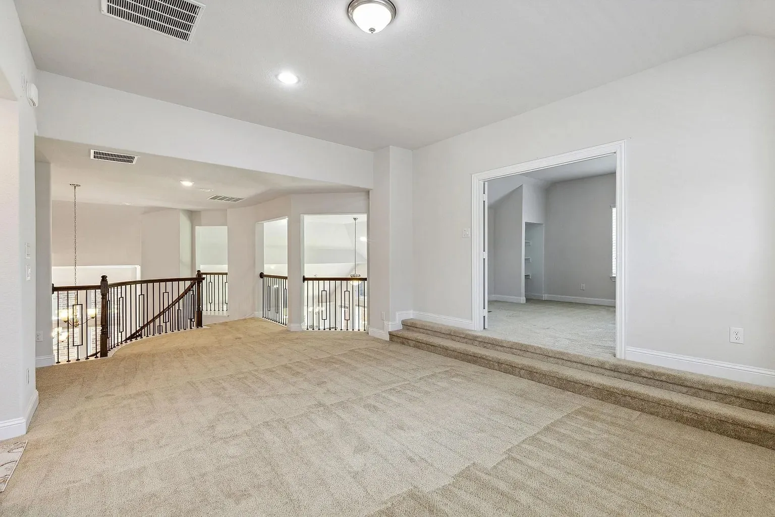 Carpeted upper-level landing featuring a wood and wrought iron staircase railing, recessed lighting, a flush mount ceiling fixture, and a carpeted two-step entry to an interior room