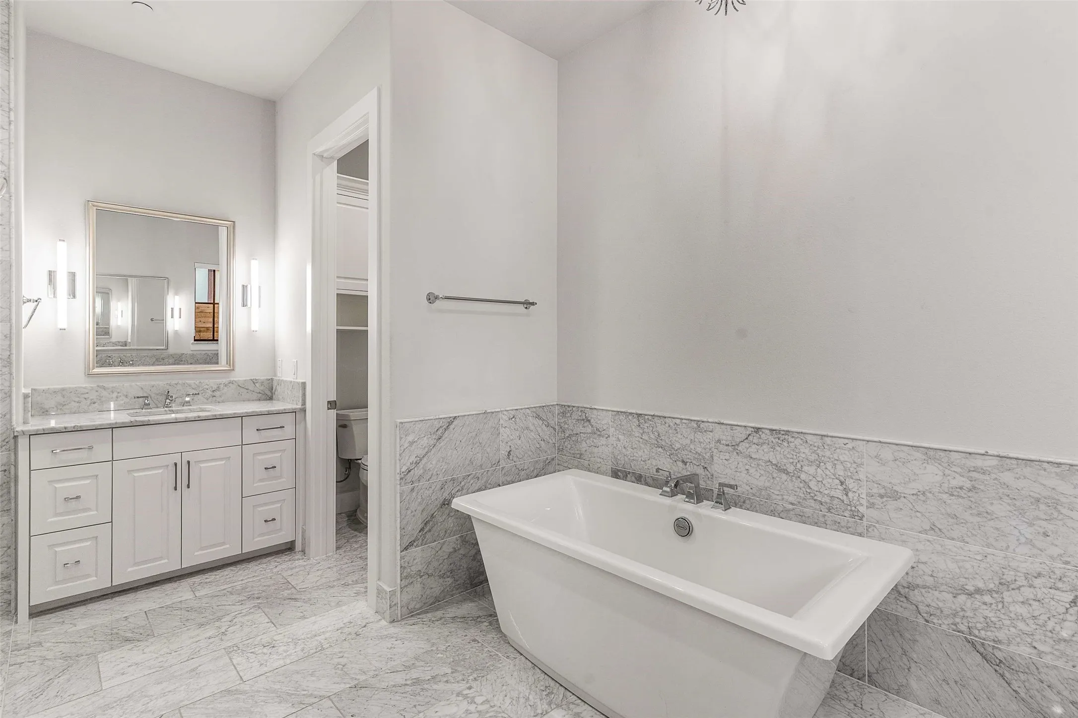 Bathroom featuring a freestanding soaking tub, dual vanity with a stone countertop, framed mirror with sconce lighting, and large format stone tile flooring