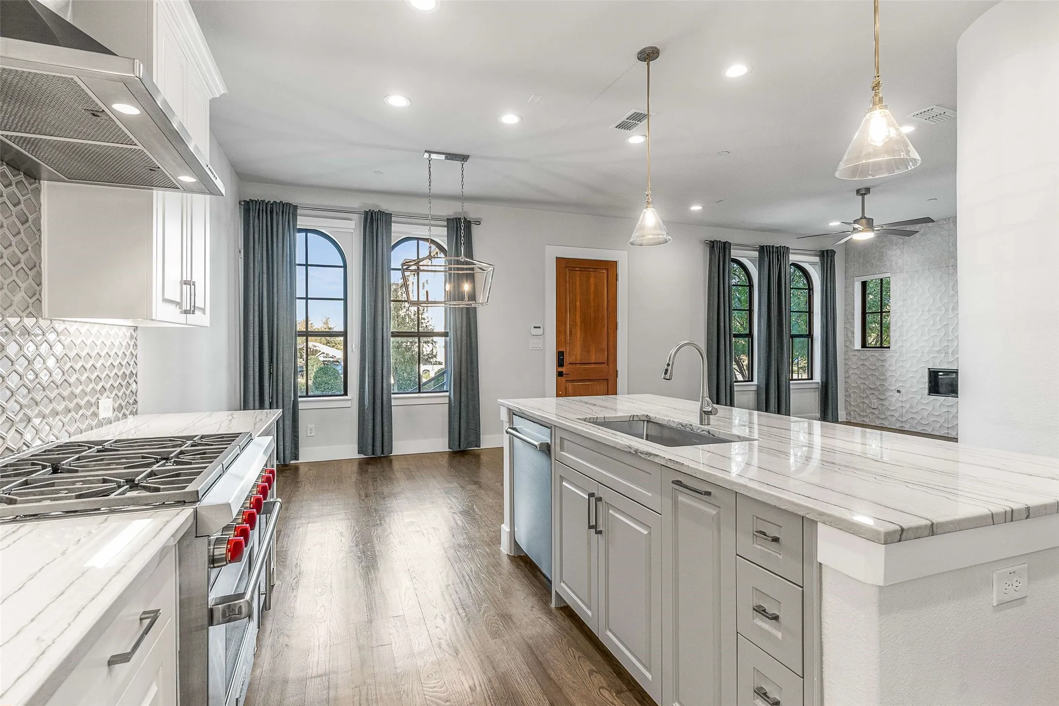 Kitchen featuring a gas range, stainless steel hood, patterned tile backsplash, and light-toned cabinetry