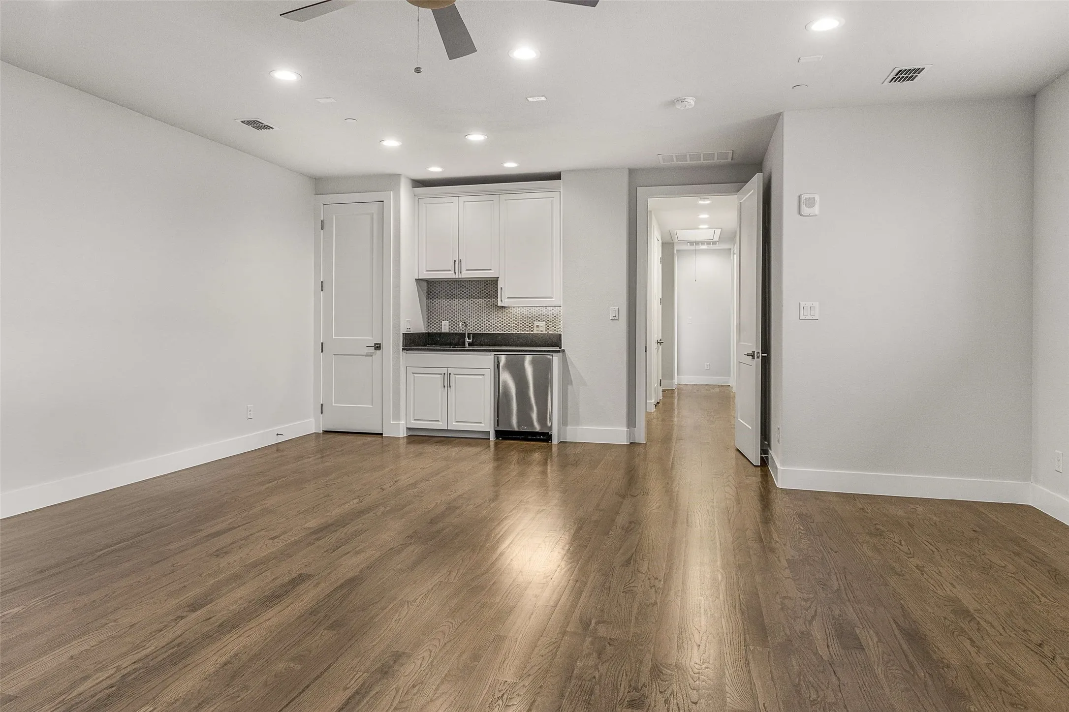 Spacious upstairs bonus room featuring wood-finish flooring, a built-in wet bar with white cabinetry and stainless steel appliances, recessed lighting, and a ceiling fan