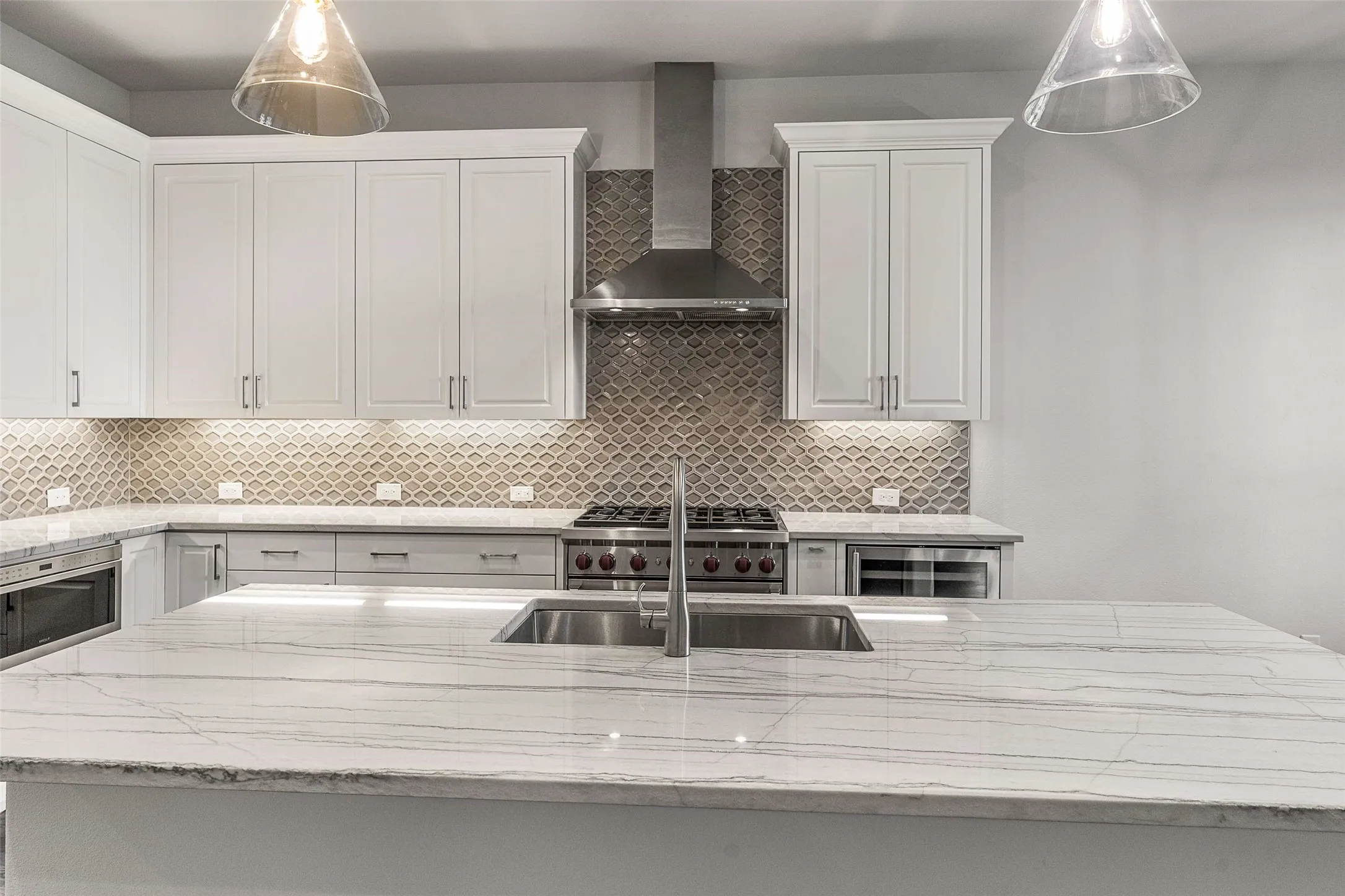 Kitchen island with a stainless steel undermount sink, white countertops, white upper cabinetry, a patterned backsplash, and stainless steel appliances