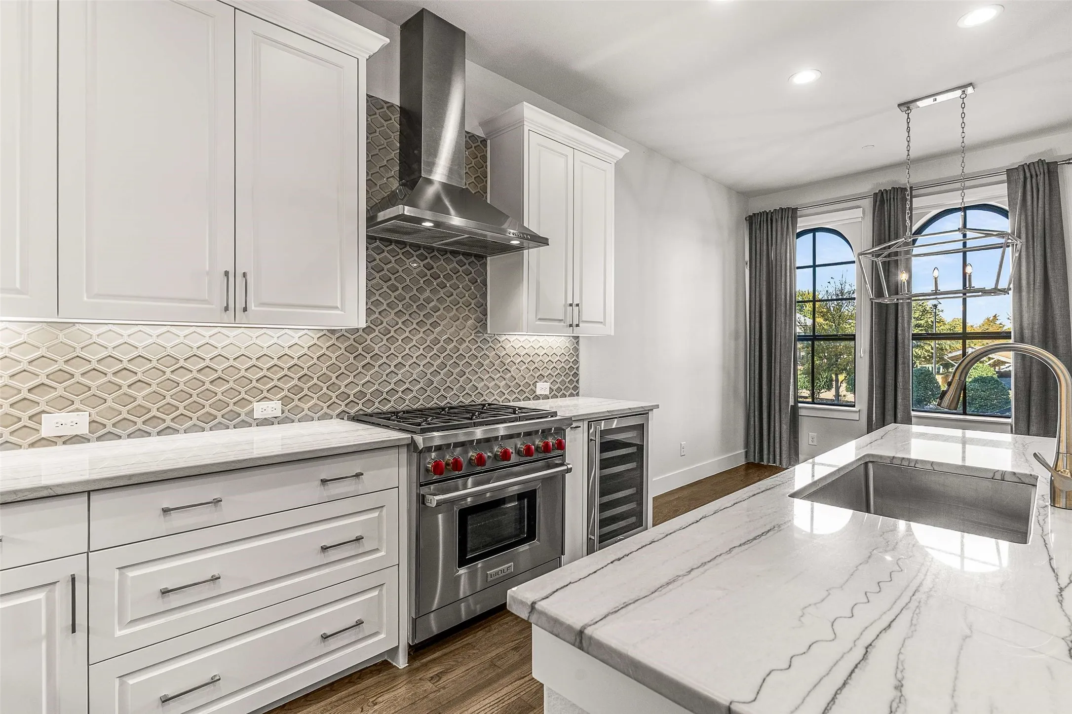 Modern kitchen featuring white shaker cabinetry, stainless steel appliances, a decorative tile backsplash, white countertops with natural veining, and hardwood flooring