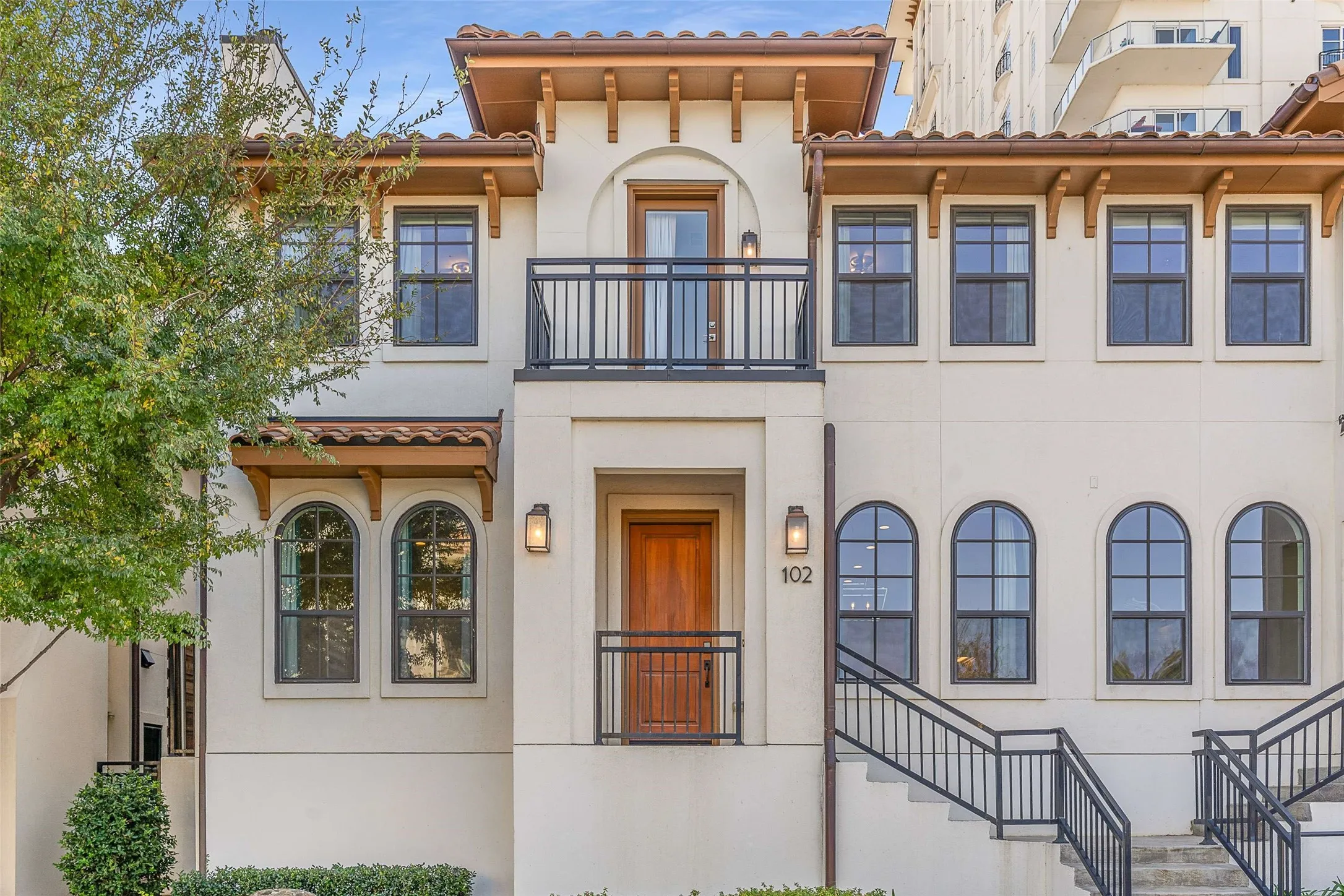 Stucco exterior featuring a tile roof, dual balconies with iron railings, arched and rectangular windows, and a wood entry door with sconce lighting