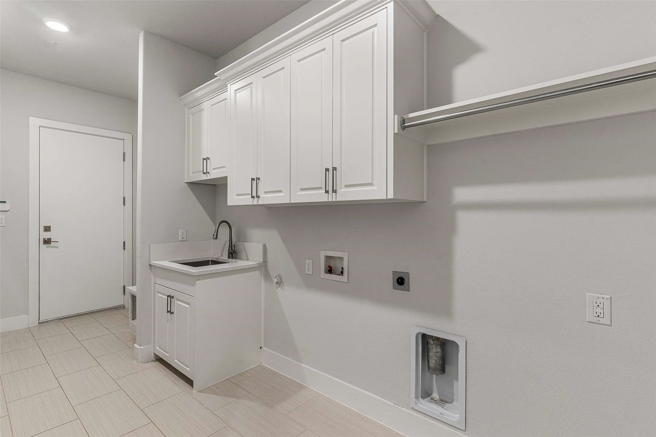 Dedicated laundry space featuring white shaker cabinetry, an integrated utility sink with a gooseneck faucet, light-toned tile flooring, and an overhead clothes rod