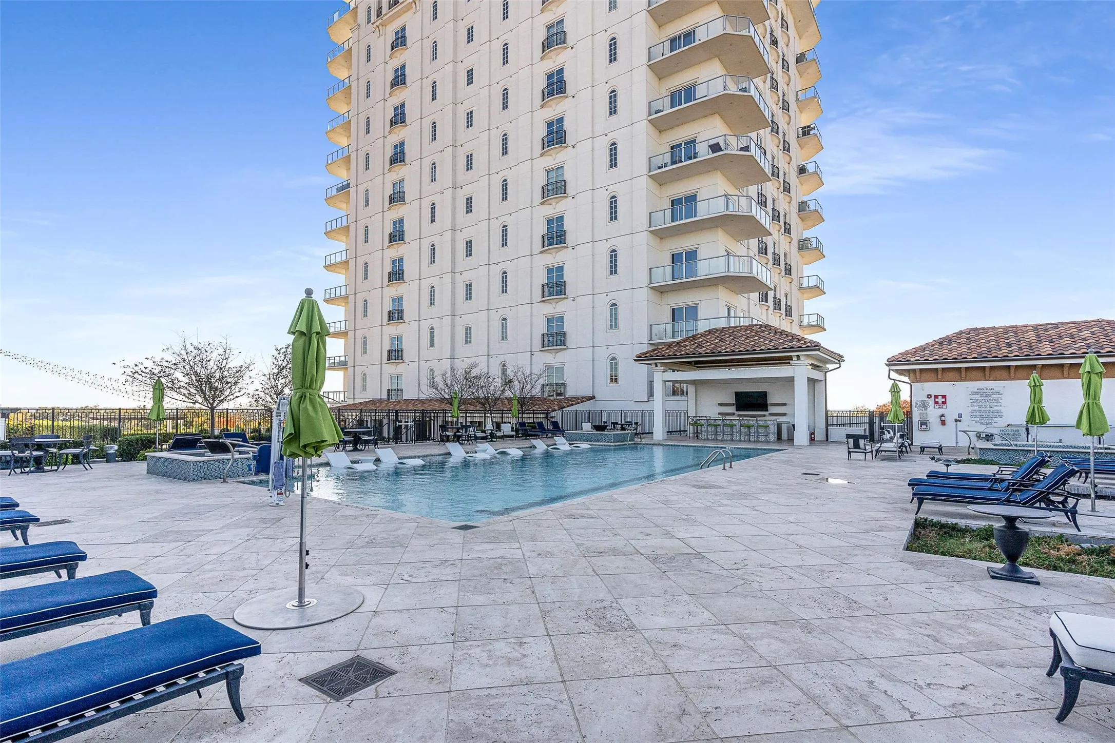Expansive outdoor pool deck featuring a large swimming pool, a covered bar area with a built-in television, and a separate building with a terracotta tile roof