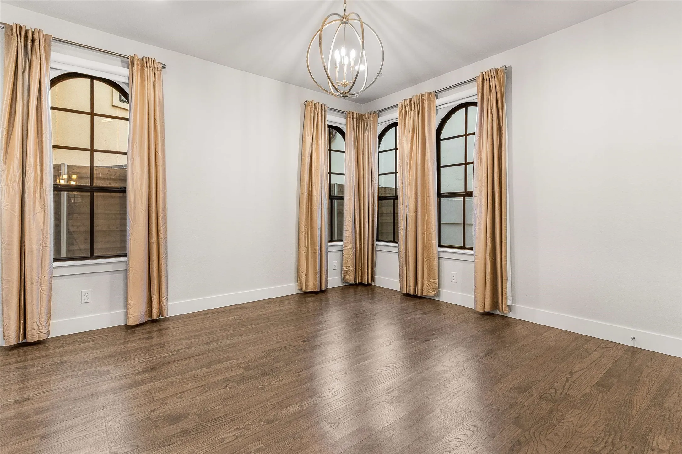 Spacious room featuring wood-finish flooring, white walls, and multiple arched windows with dark framing