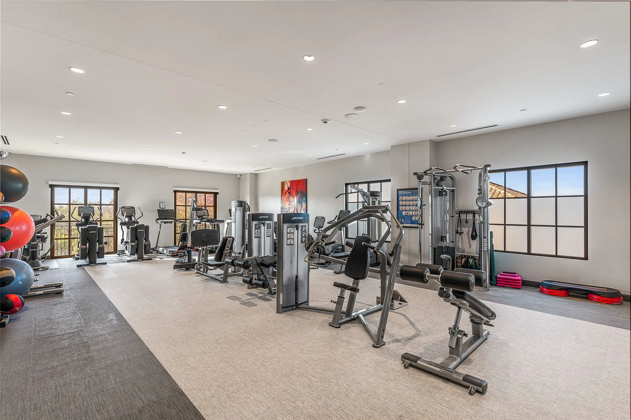 COmmunity Fitness center featuring multiple exercise machines, recessed lighting, large windows with dark frames, light-colored walls, and a multi-toned floor