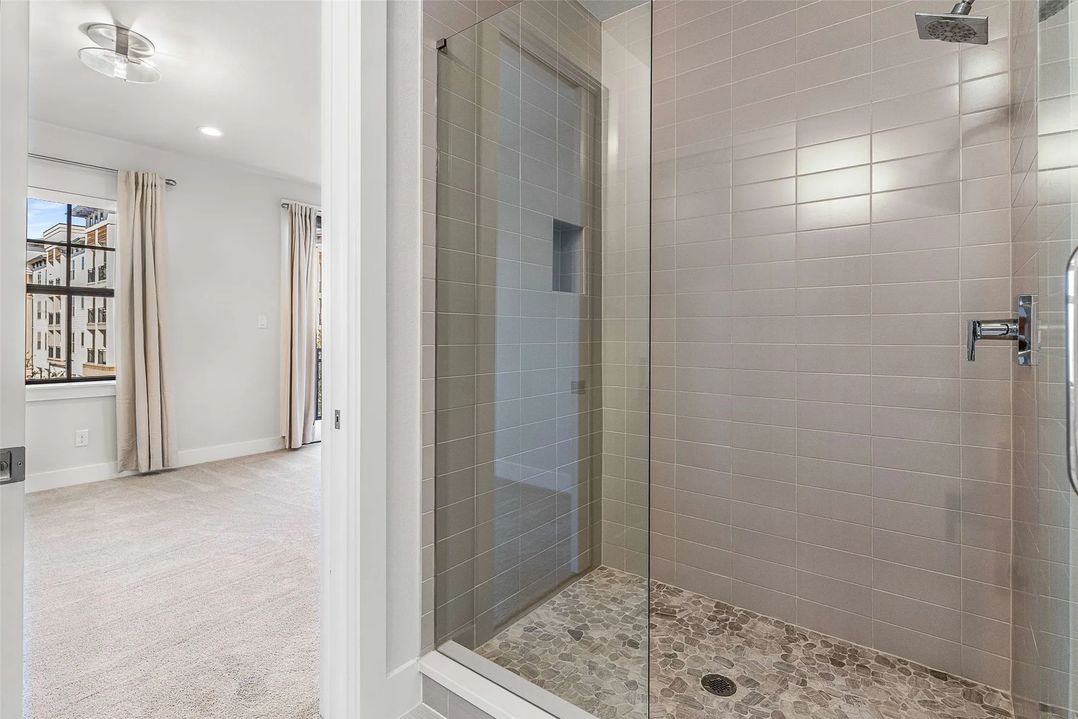 Glass-enclosed shower featuring horizontal subway tile, a recessed niche, and a river rock floor