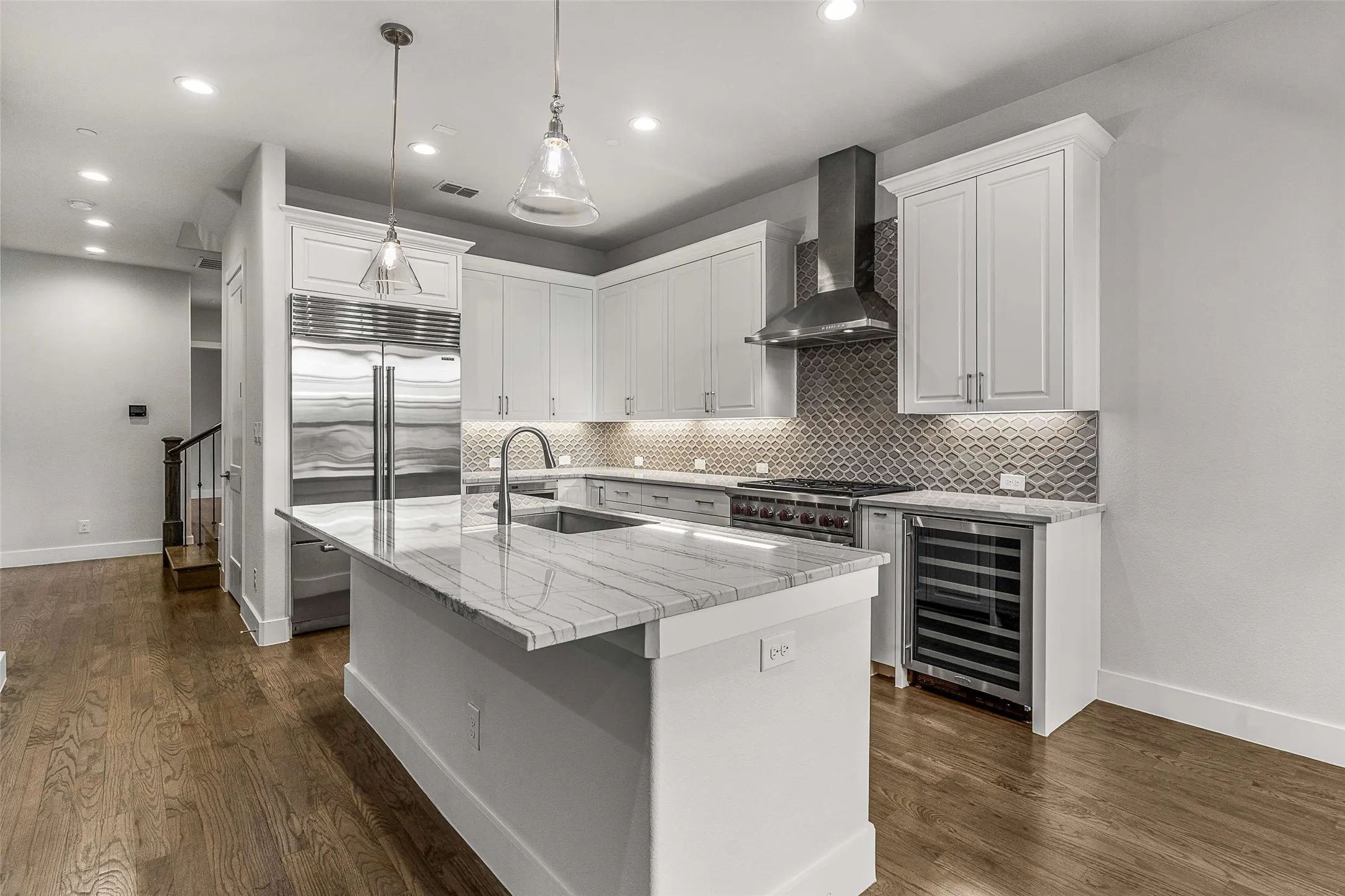 Gourmet kitchen featuring a large central island with a sink, stainless steel appliances, white cabinetry, a decorative tile backsplash, and wood-finish flooring