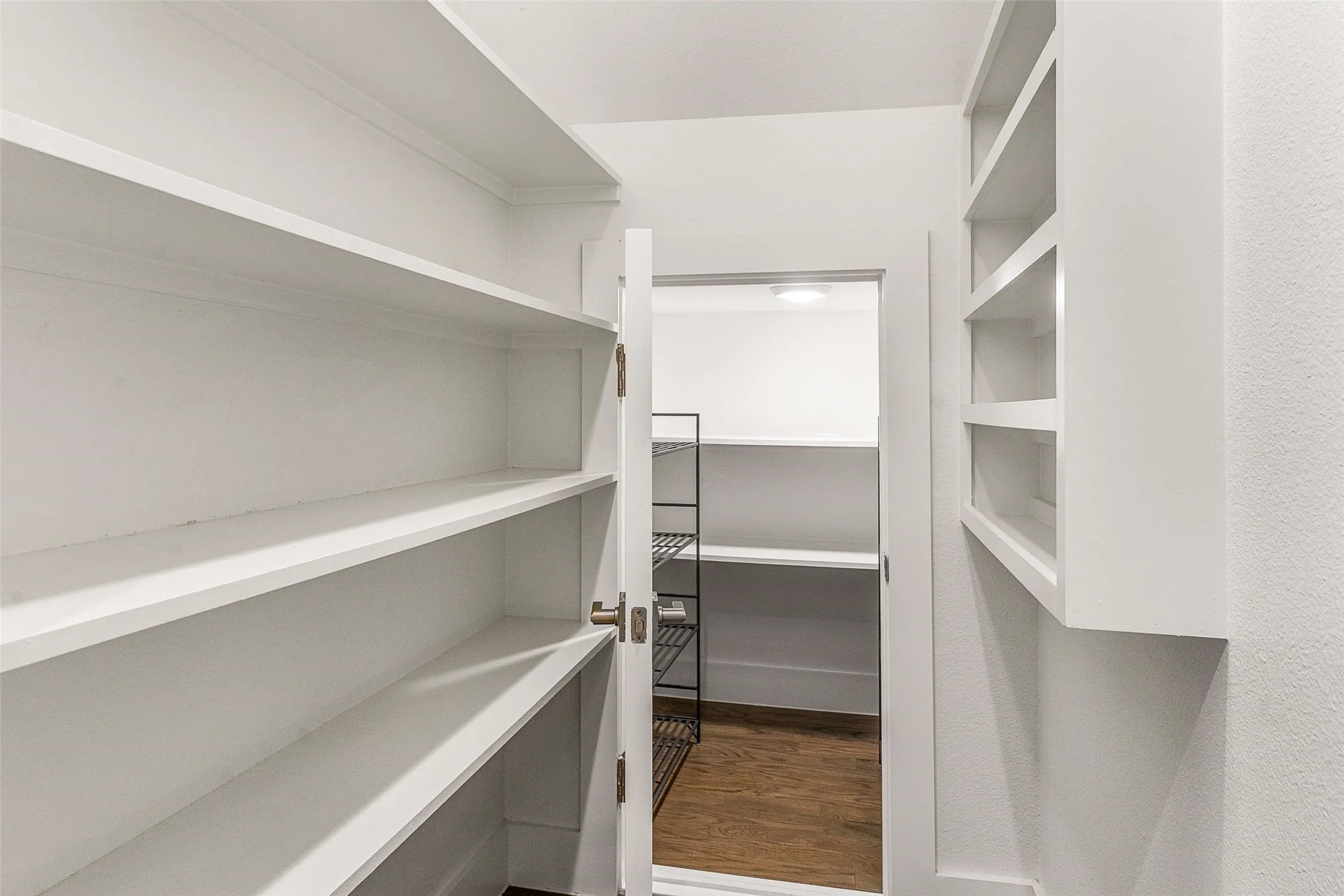 Walk-in pantry featuring extensive built-in shelving, white painted cabinetry, and wood-finish flooring