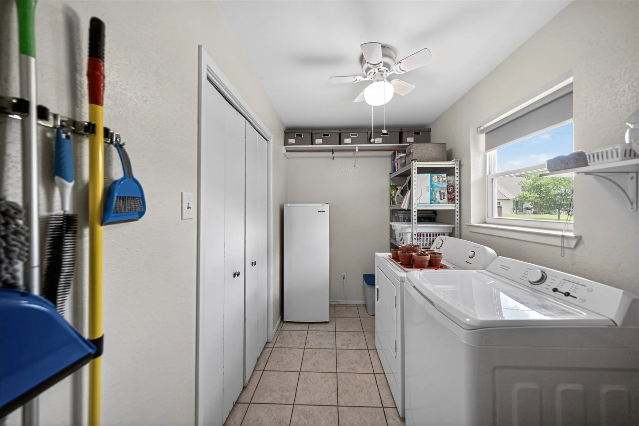 Dedicated utility space featuring tile flooring, built-in shelving, a ceiling fan with integrated lighting, and a window providing natural illumination
