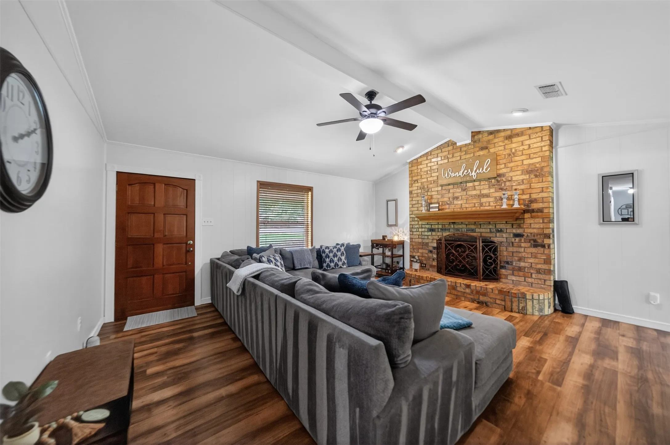 Living space featuring a brick fireplace with a wood mantle, wood-finish flooring, and a vaulted ceiling with a ceiling fan