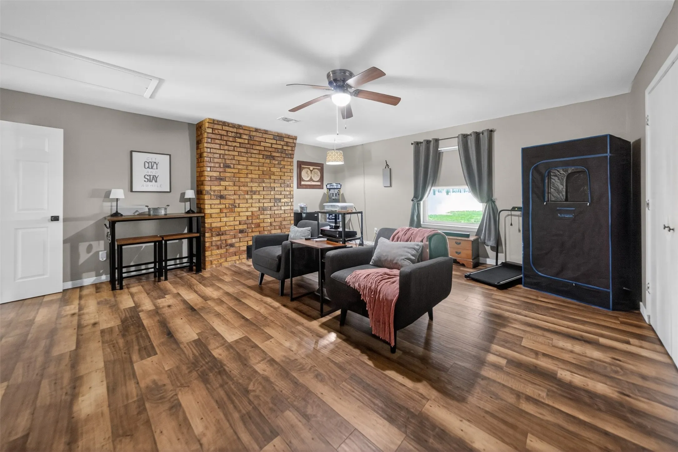 Spacious room featuring wood-finish flooring, a prominent exposed brick accent wall, and neutral wall tones