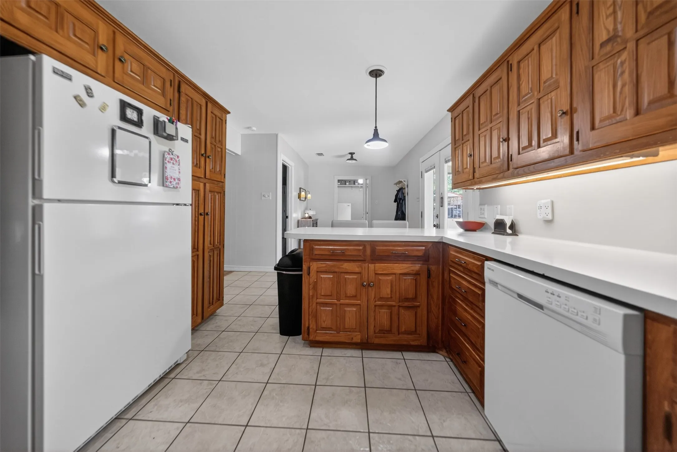Kitchen featuring extensive wood cabinetry, white countertops, tile flooring, white appliances, and pendant lighting