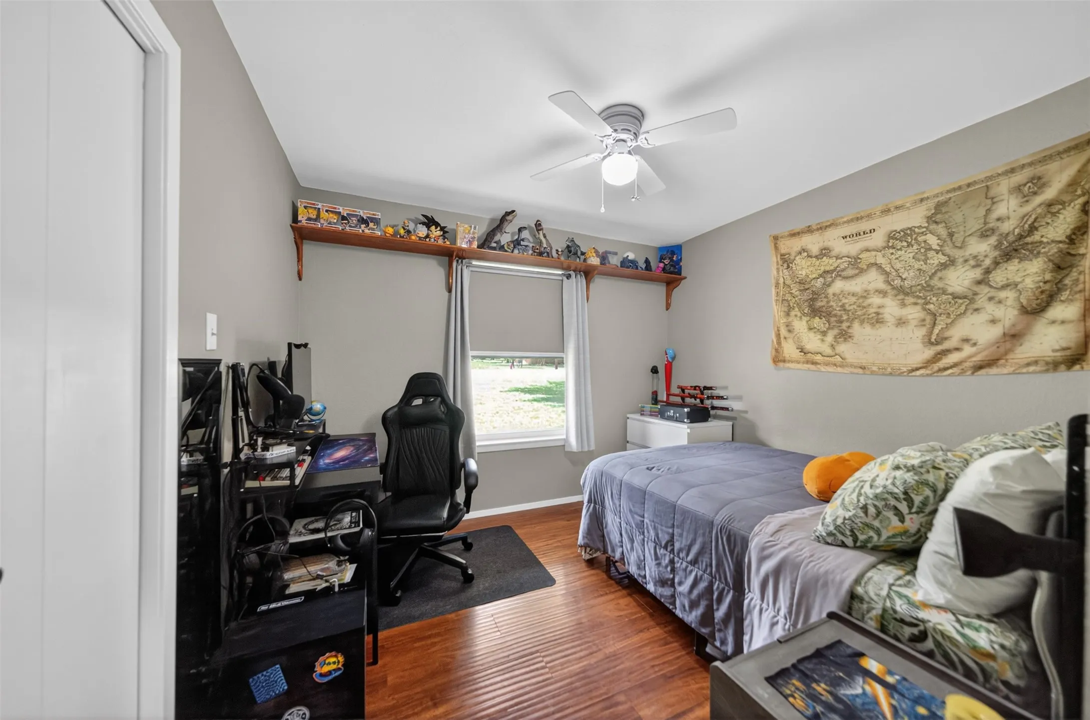 Bedroom featuring wood-finish flooring, a contemporary ceiling fan with integrated lighting, a single window with blinds, and built-in wall shelving
