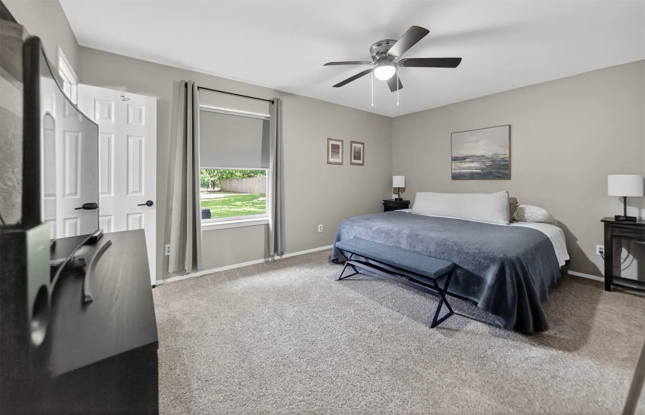 Carpeted bedroom featuring a ceiling fan with integrated lighting, a window with roller shade, and a paneled door with dark hardware
