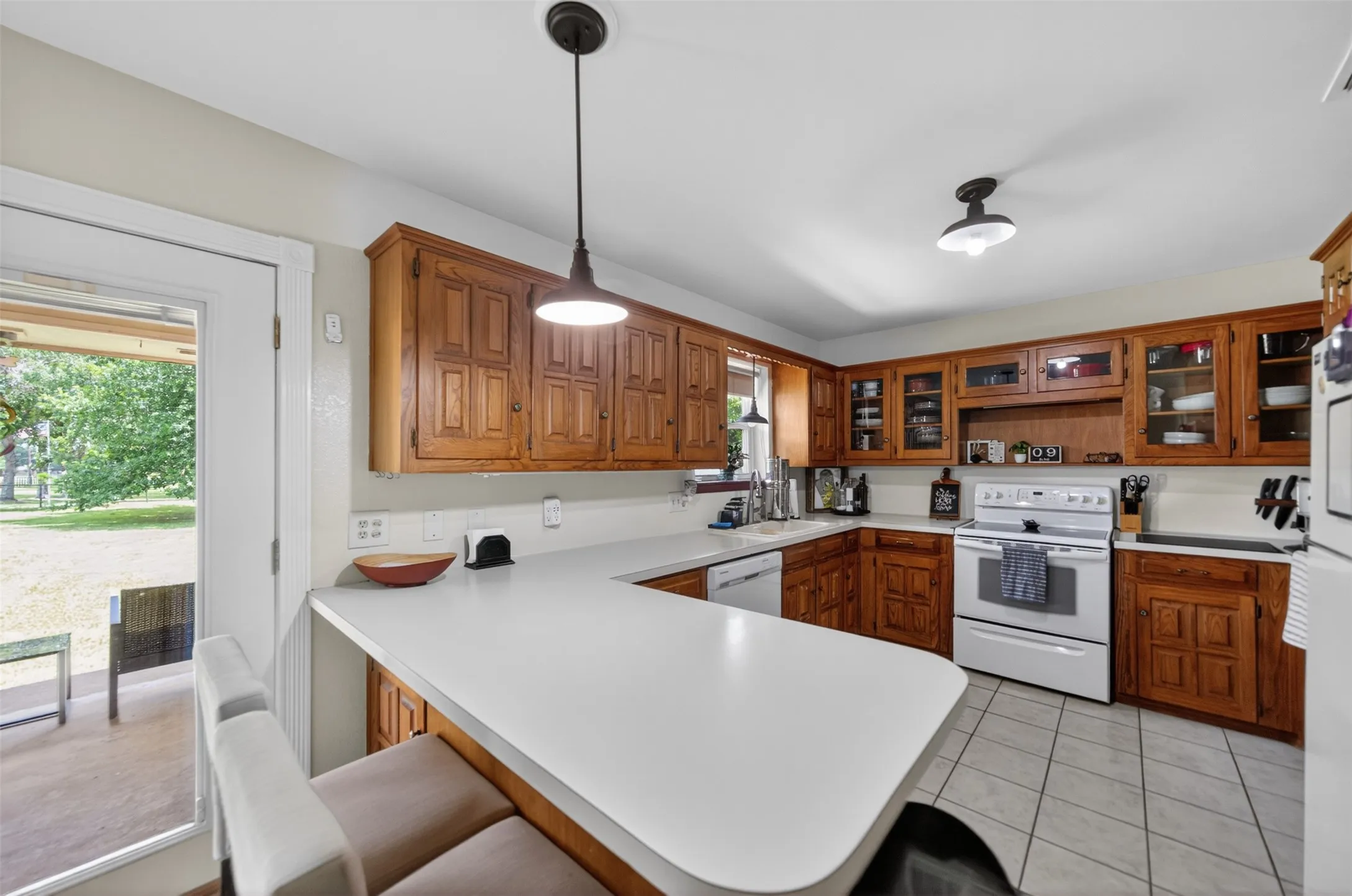 Kitchen featuring wood cabinetry, white countertops, tile flooring, and white appliances