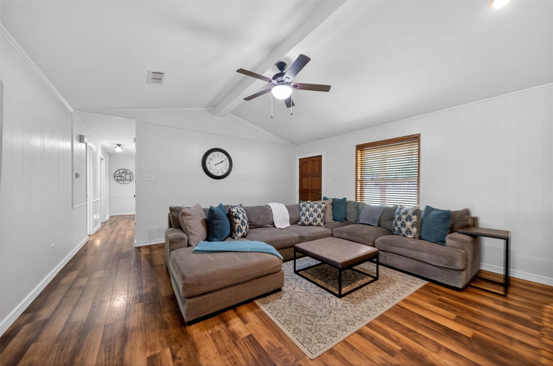 Living area featuring wood-finish flooring, a vaulted ceiling with exposed beams, and a ceiling fan with integrated lighting