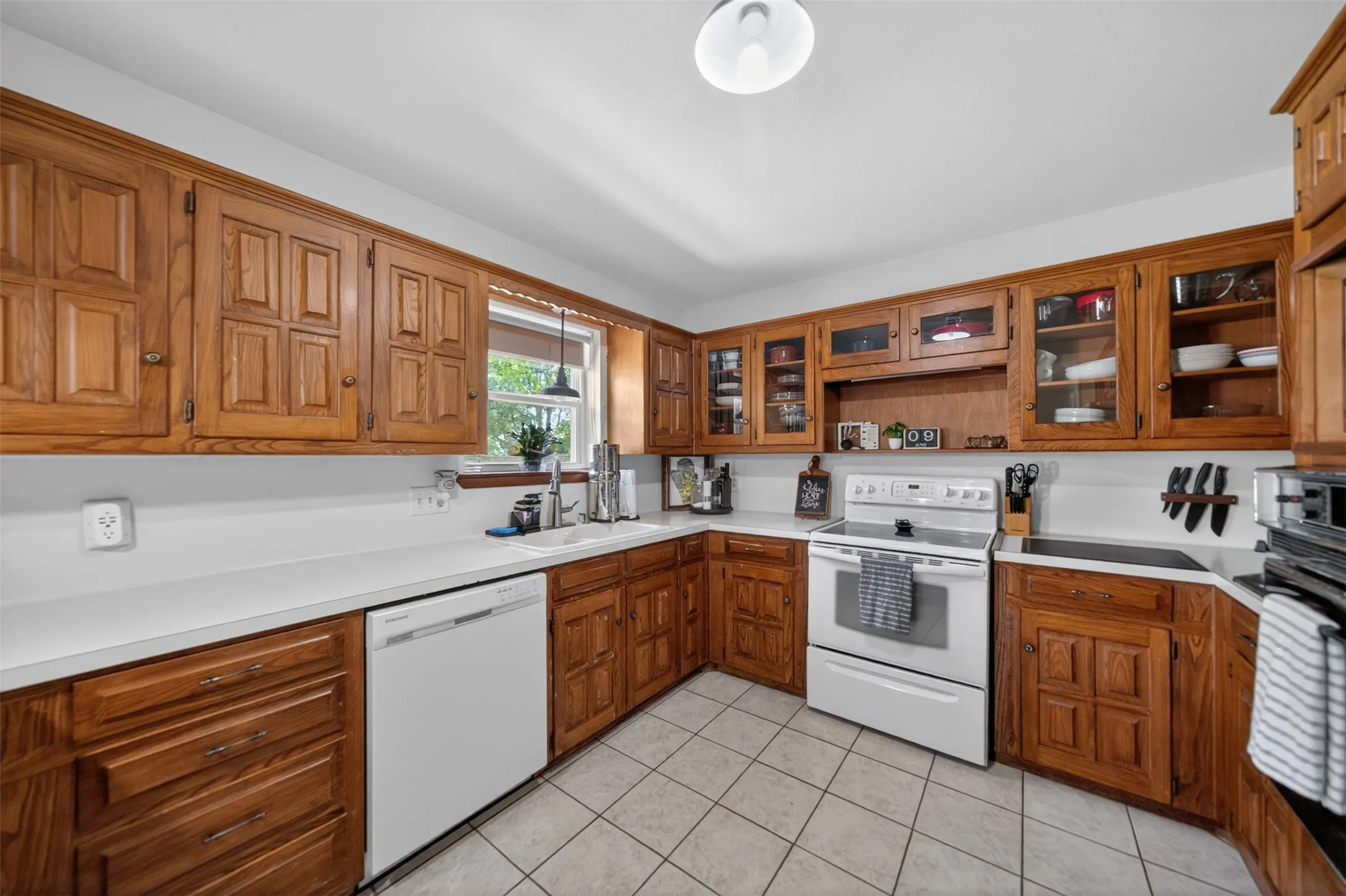 Kitchen featuring extensive wood cabinetry, white countertops, white tile flooring, and a white appliance package including a range and dishwasher