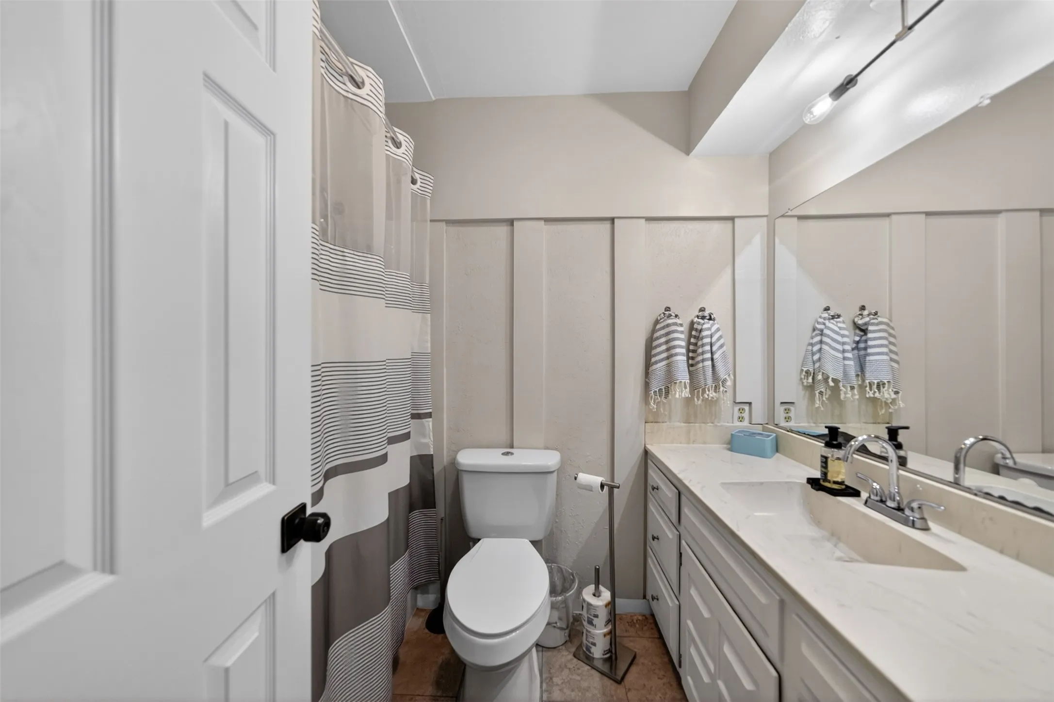 Bathroom featuring a single vanity with built-in cabinetry, an integrated sink, and a large wall-mounted mirror