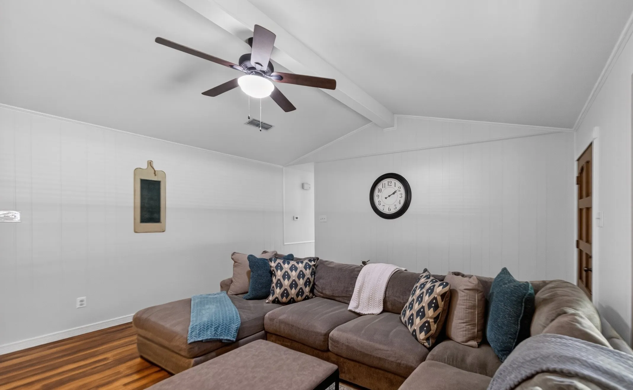 Vaulted ceiling with exposed beams, ceiling fan light fixture, wood-finish flooring, and white paneled walls