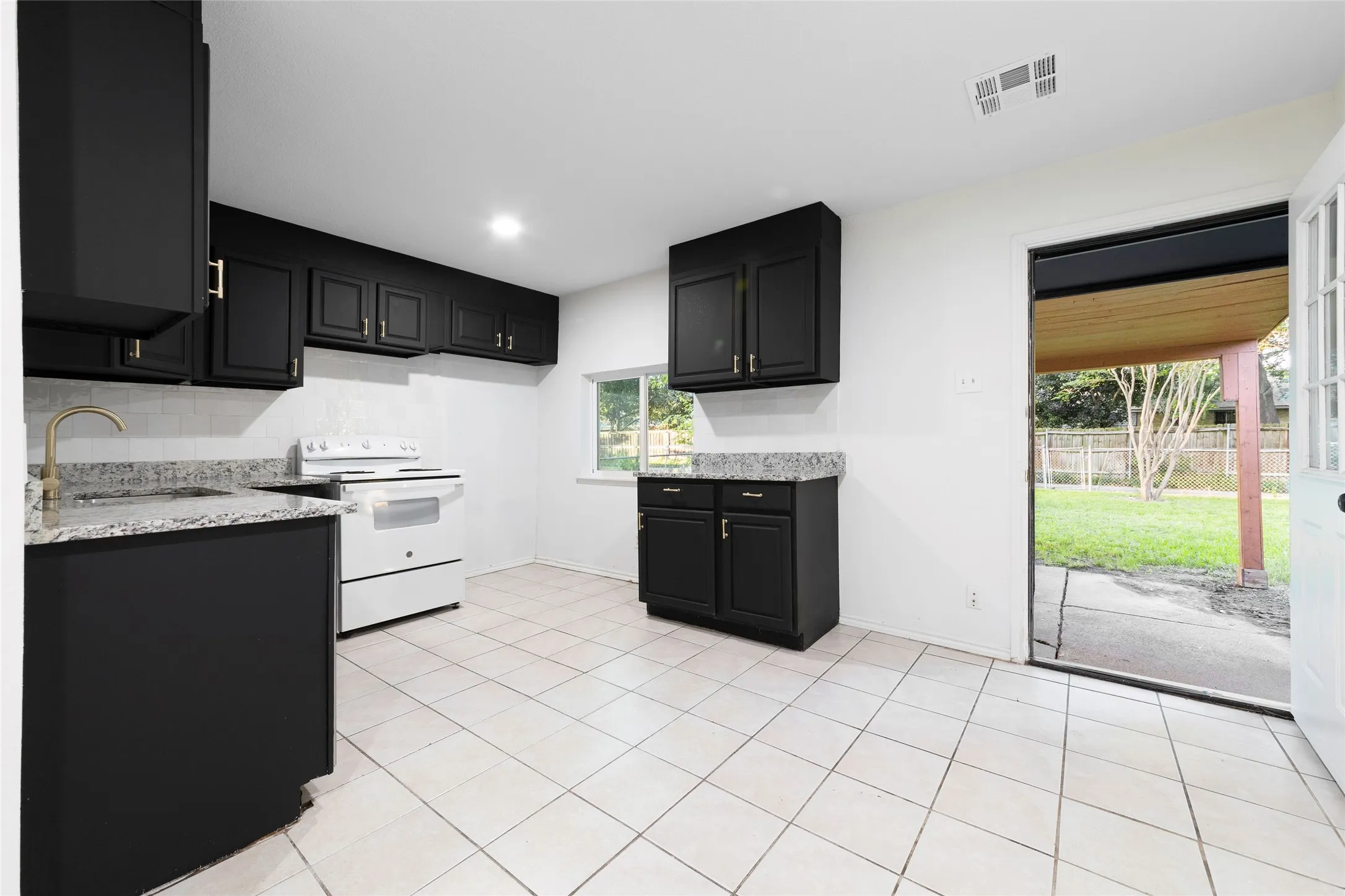 Kitchen featuring black cabinetry with gold-toned hardware, speckled countertops, a white tile backsplash, and a white electric range