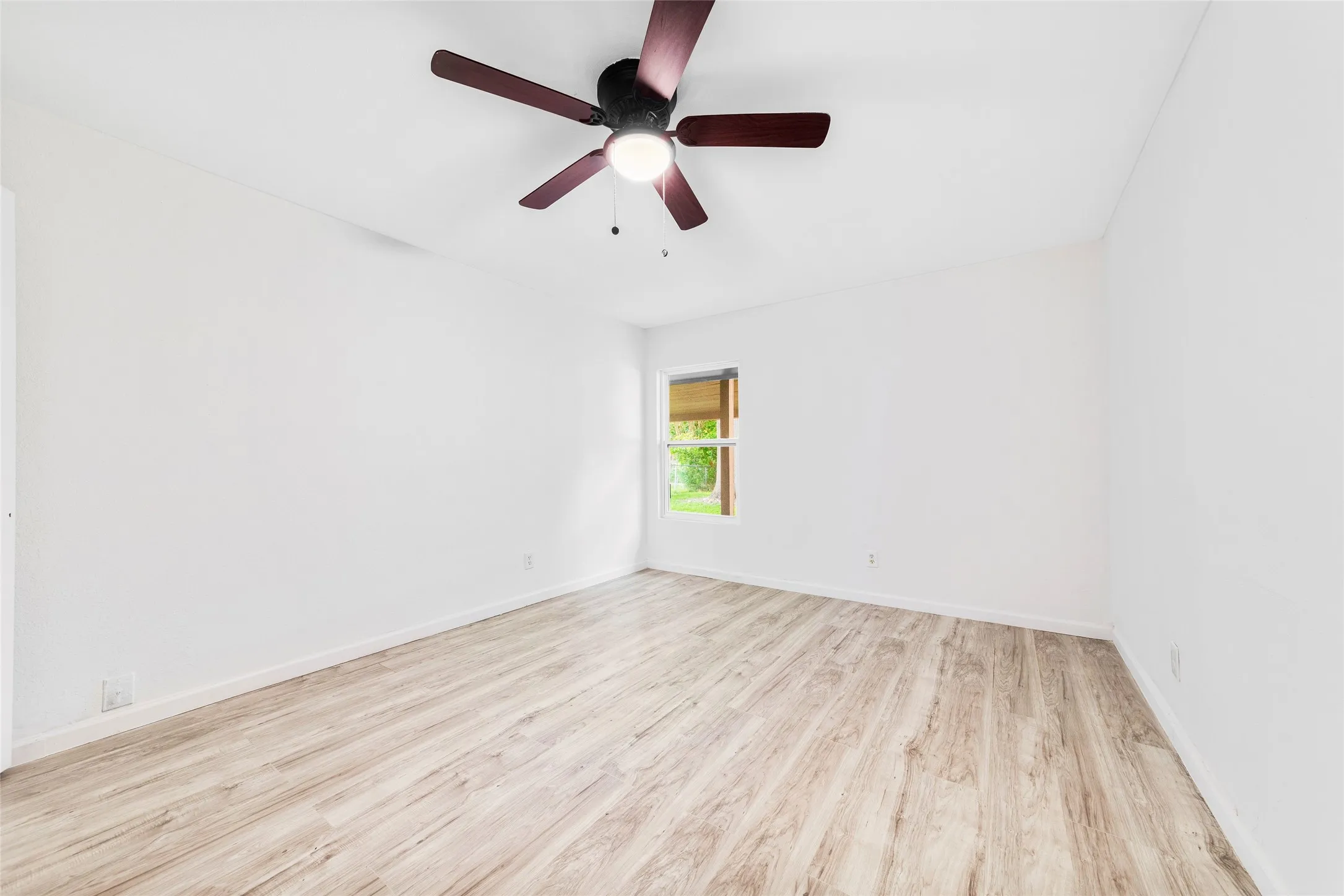 Spacious room featuring wood-finish flooring, white walls, and a ceiling fan with integrated lighting