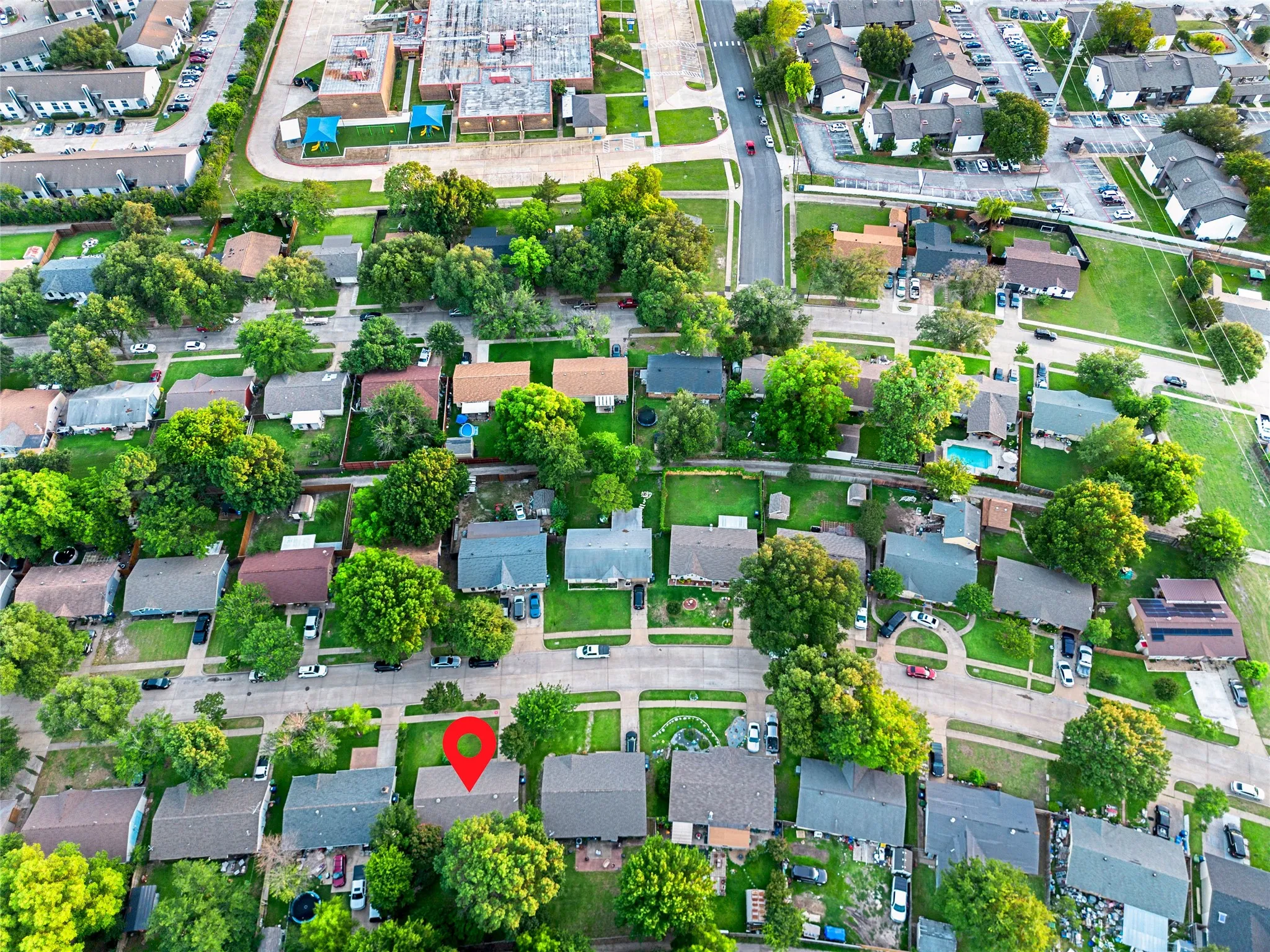 Aerial view of a residential neighborhood featuring numerous single-family homes with pitched roofs, mature trees, and visible street access