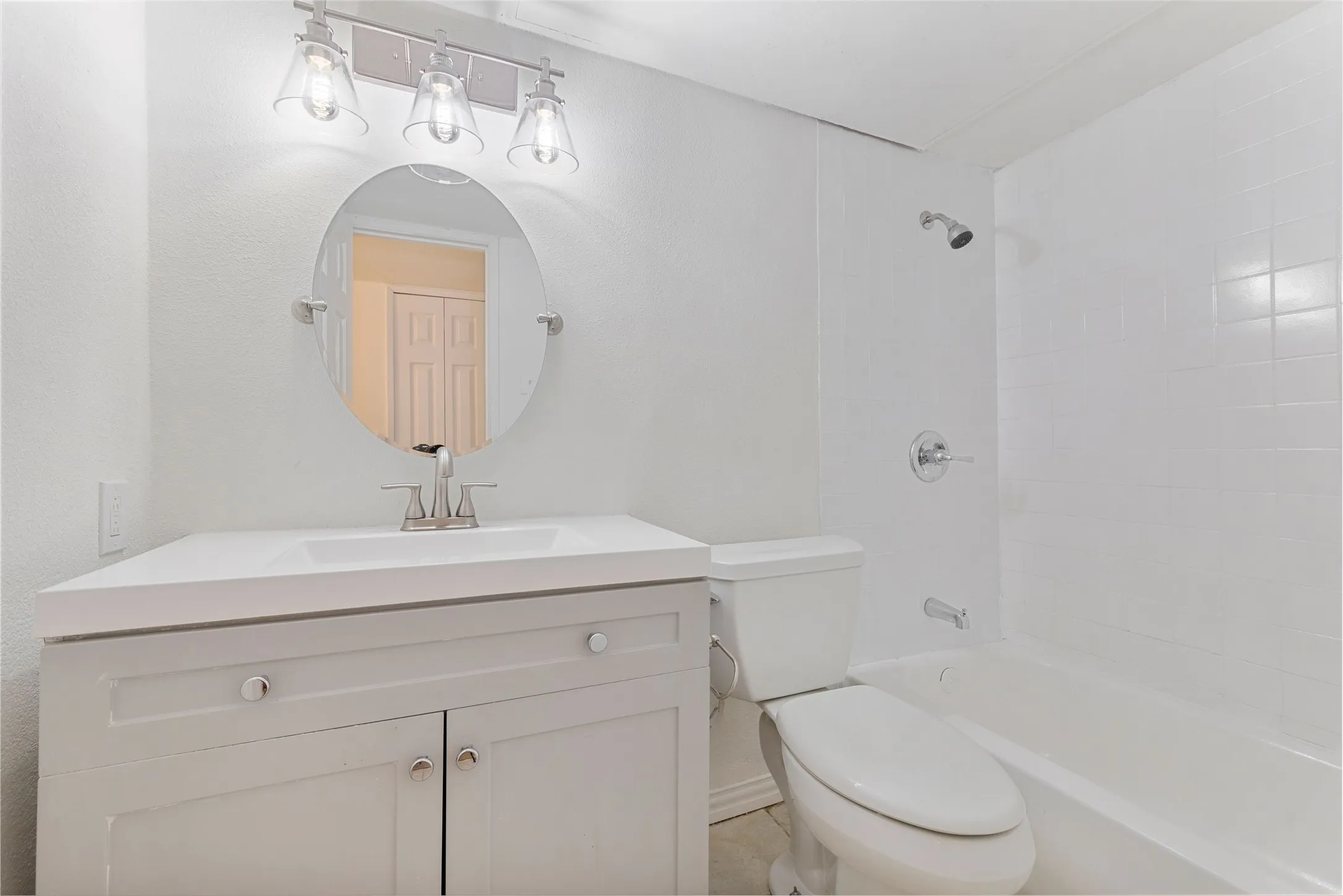 Bathroom featuring a white vanity with integrated sink, chrome faucet, and circular mirror