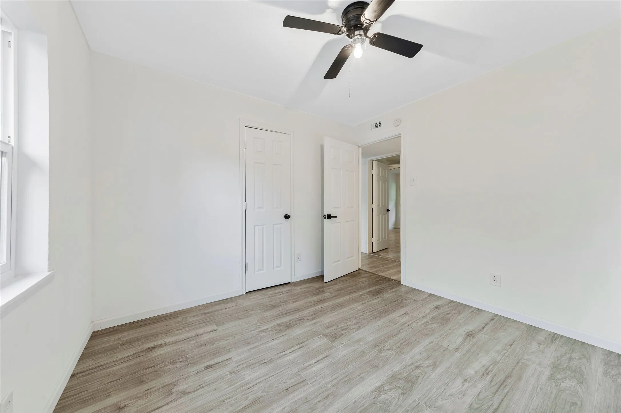 Spacious room featuring wood-finish flooring, white walls, and a ceiling fan