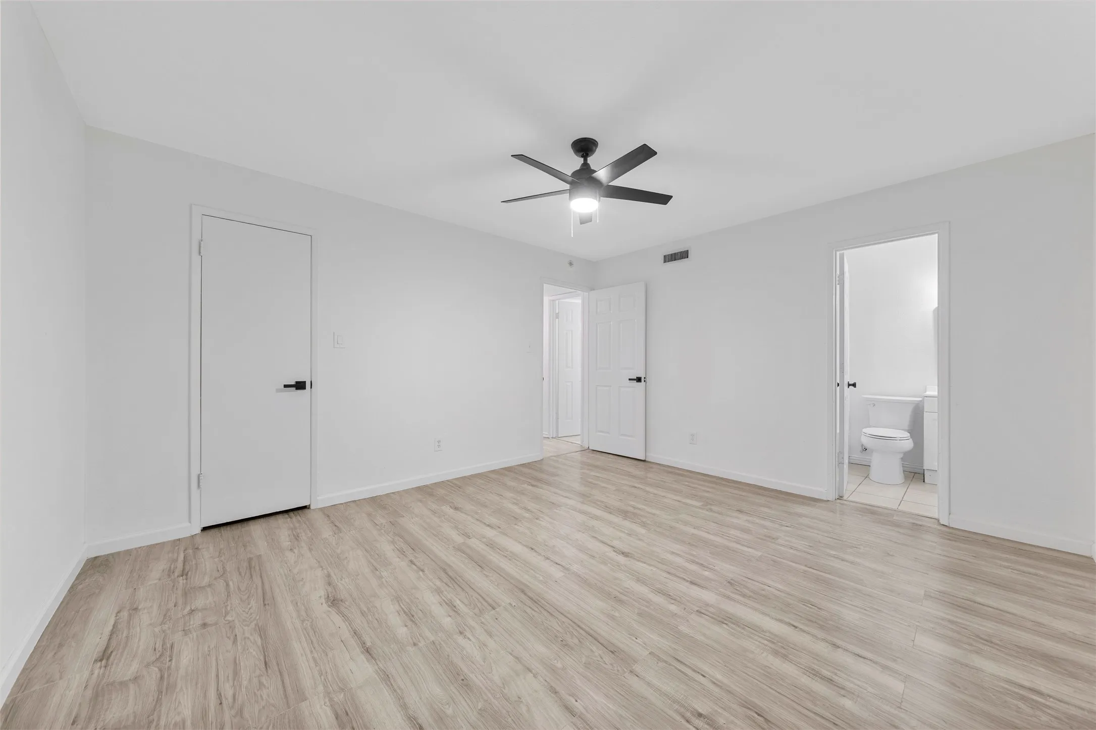 Spacious interior featuring light wood-finish flooring, white walls, and a contemporary ceiling fan