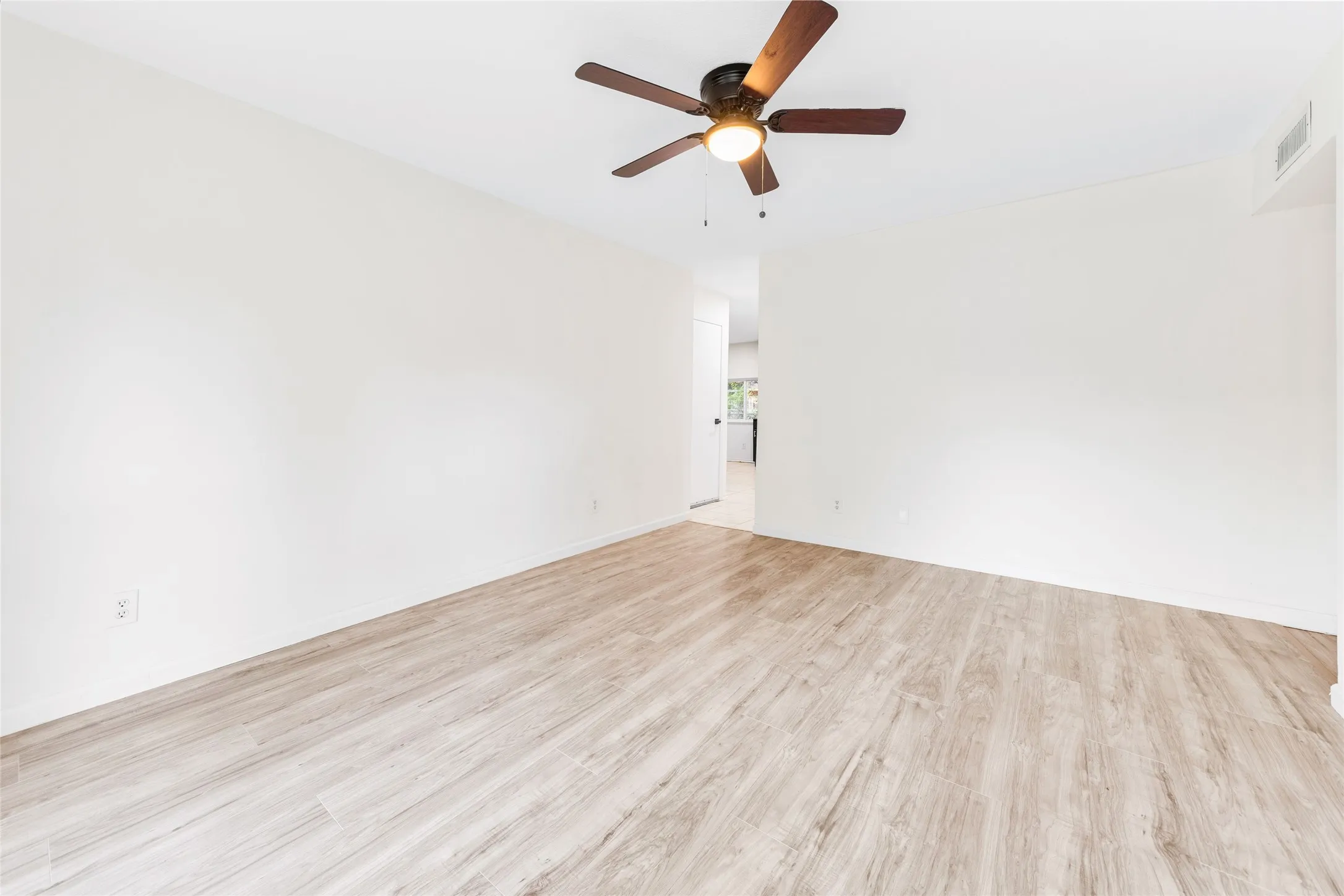 Spacious room featuring wood-finish flooring and a ceiling fan with integrated lighting