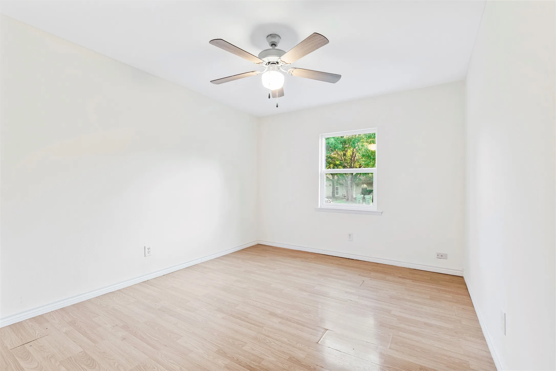Bright room featuring wood-finish flooring, white walls, and a ceiling fan with integrated lighting