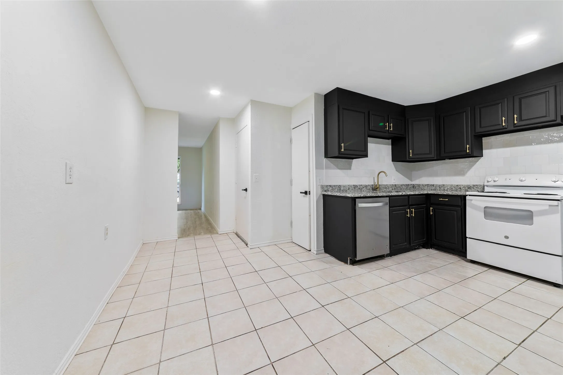 Kitchen featuring black cabinetry with gold-toned hardware, stone-look countertops, and a white tile backsplash