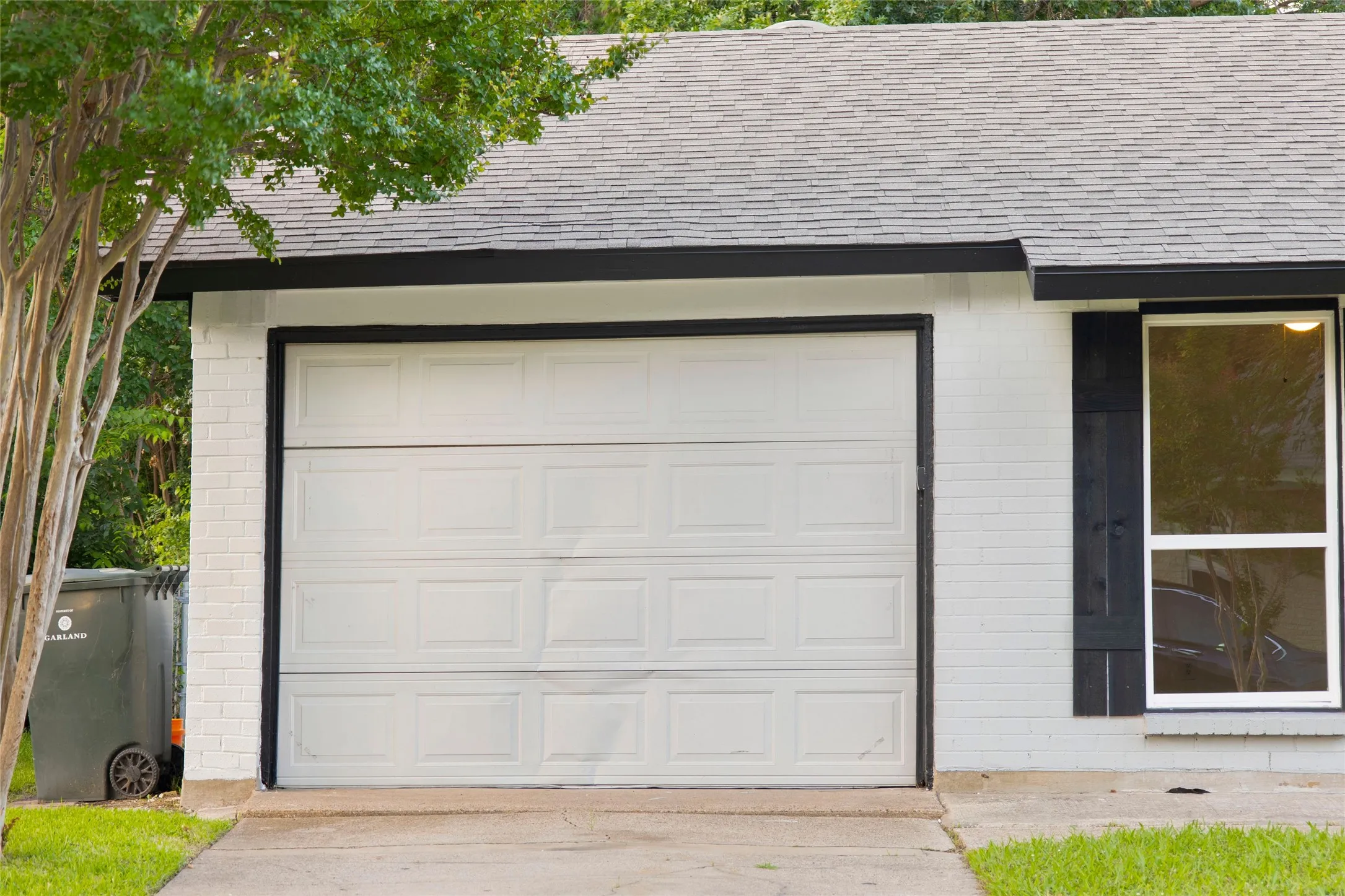 White paneled garage door with dark trim, set into a white brick facade