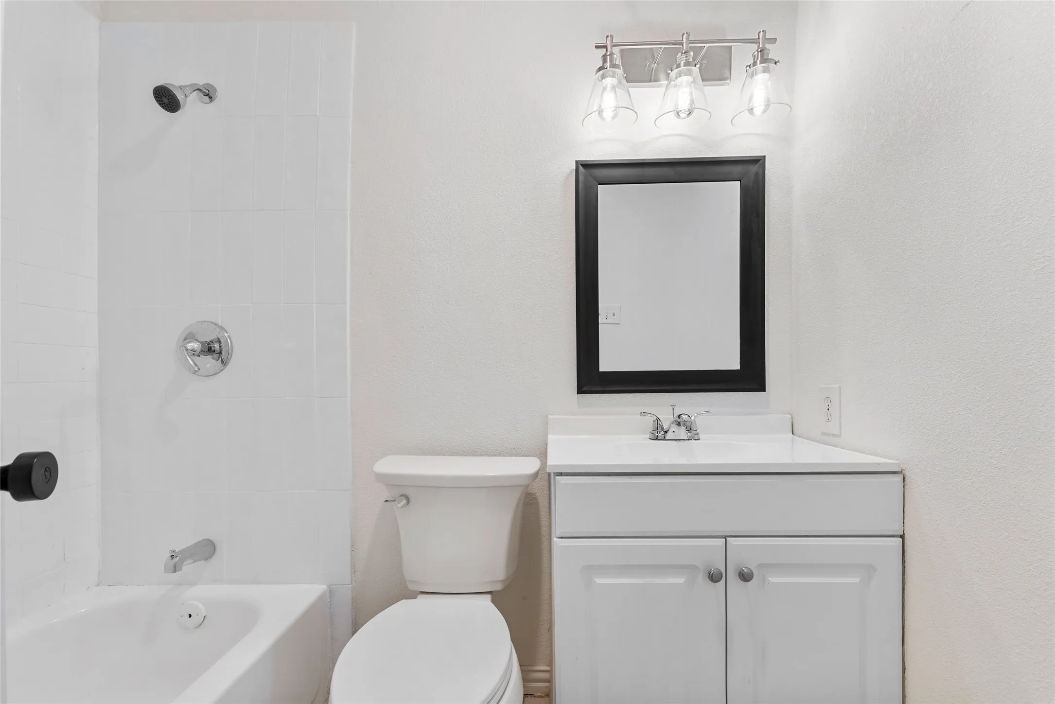 Bathroom featuring a white subway-tiled shower, chrome fixtures, white vanity with integrated sink, and a black-framed mirror with brushed nickel lighting
