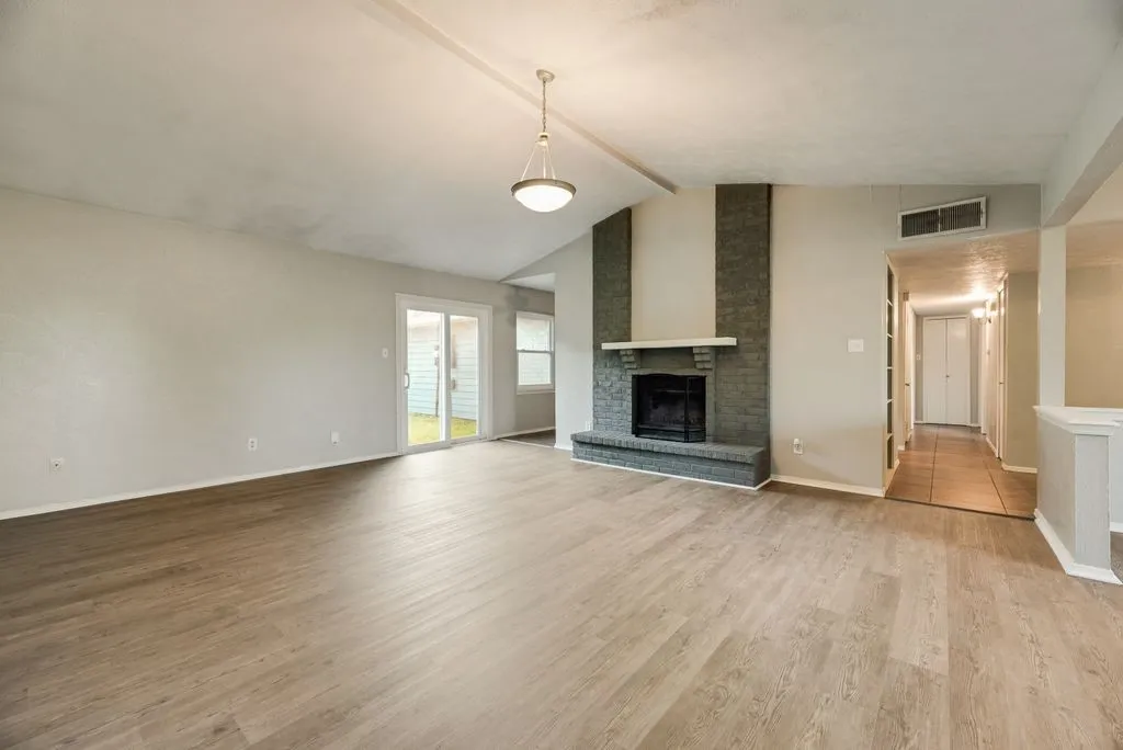 Spacious living area featuring wood-finish flooring, a brick fireplace with a mantle, and vaulted ceilings