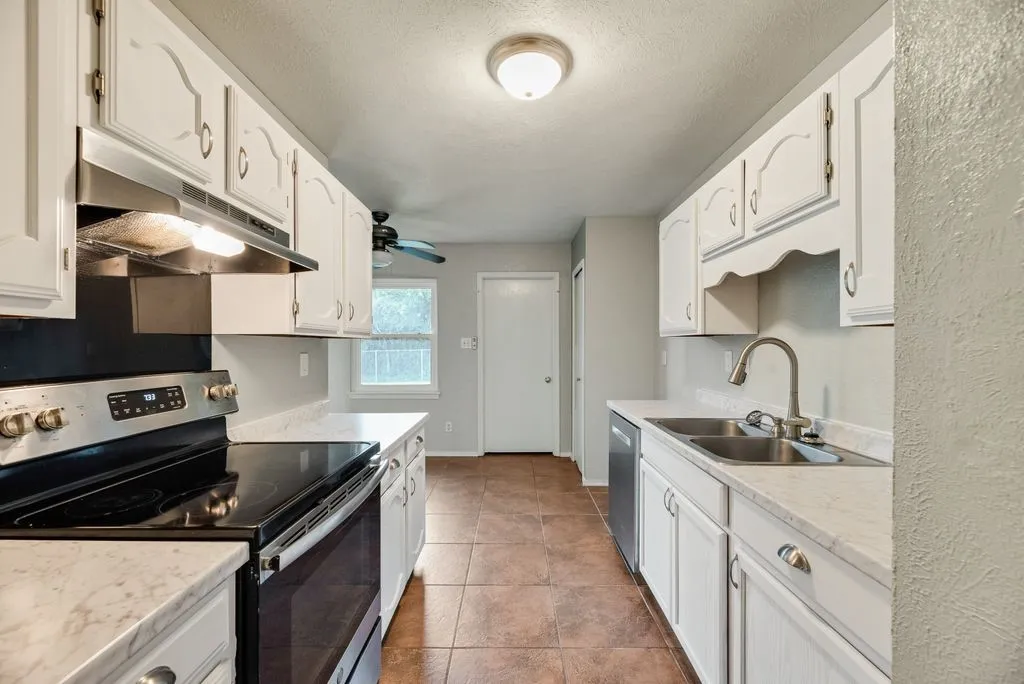 Galley kitchen featuring white cabinetry, light countertops, tile flooring, and stainless steel appliances including a range and double basin sink
