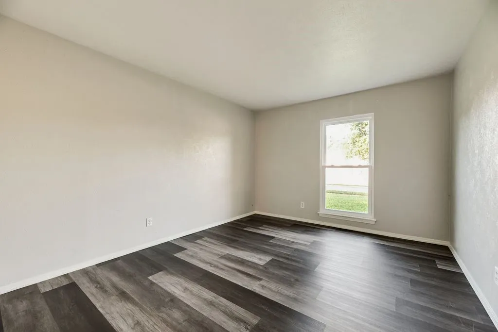 Room featuring dark wood-finish flooring, light neutral-toned walls, a white trim baseboard, a single window with white framing, and a smooth white ceiling