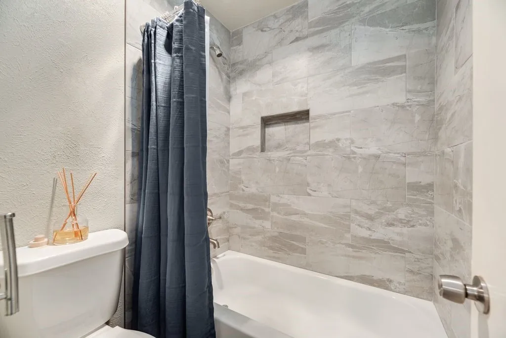 Bathtub and shower combination featuring large format grey tile surround, recessed shower niche, and brushed nickel fixtures